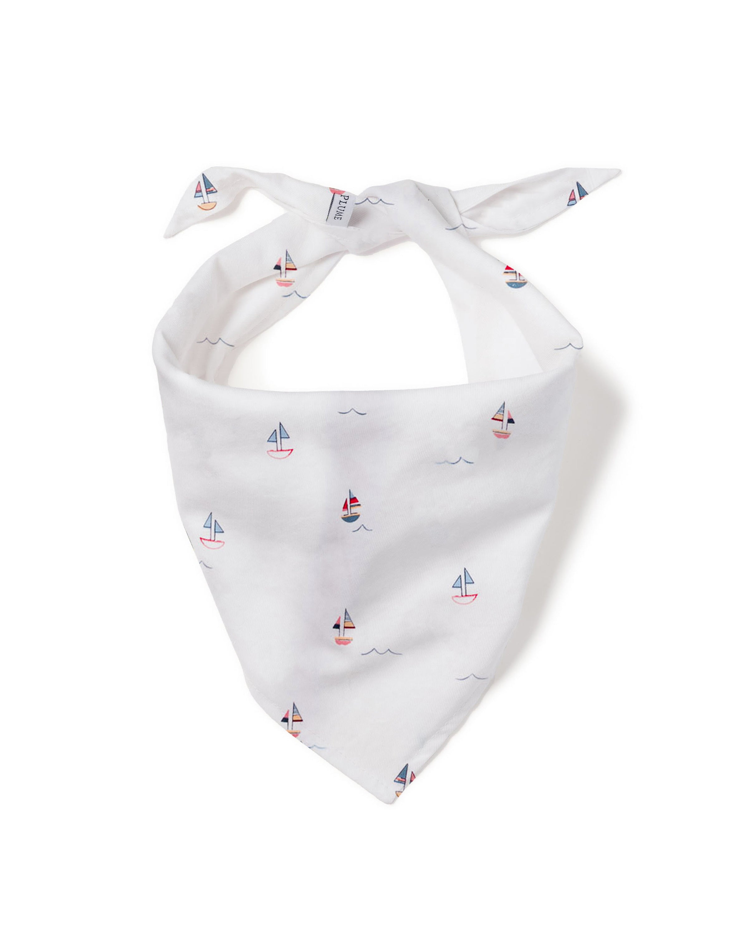A fluffy white dog sits on the wooden floor, joyfully grinning with its tongue out, wearing a Dog Twill Bandana in Bateau by Petite Plume—perfectly showcasing stylish dog accessories.