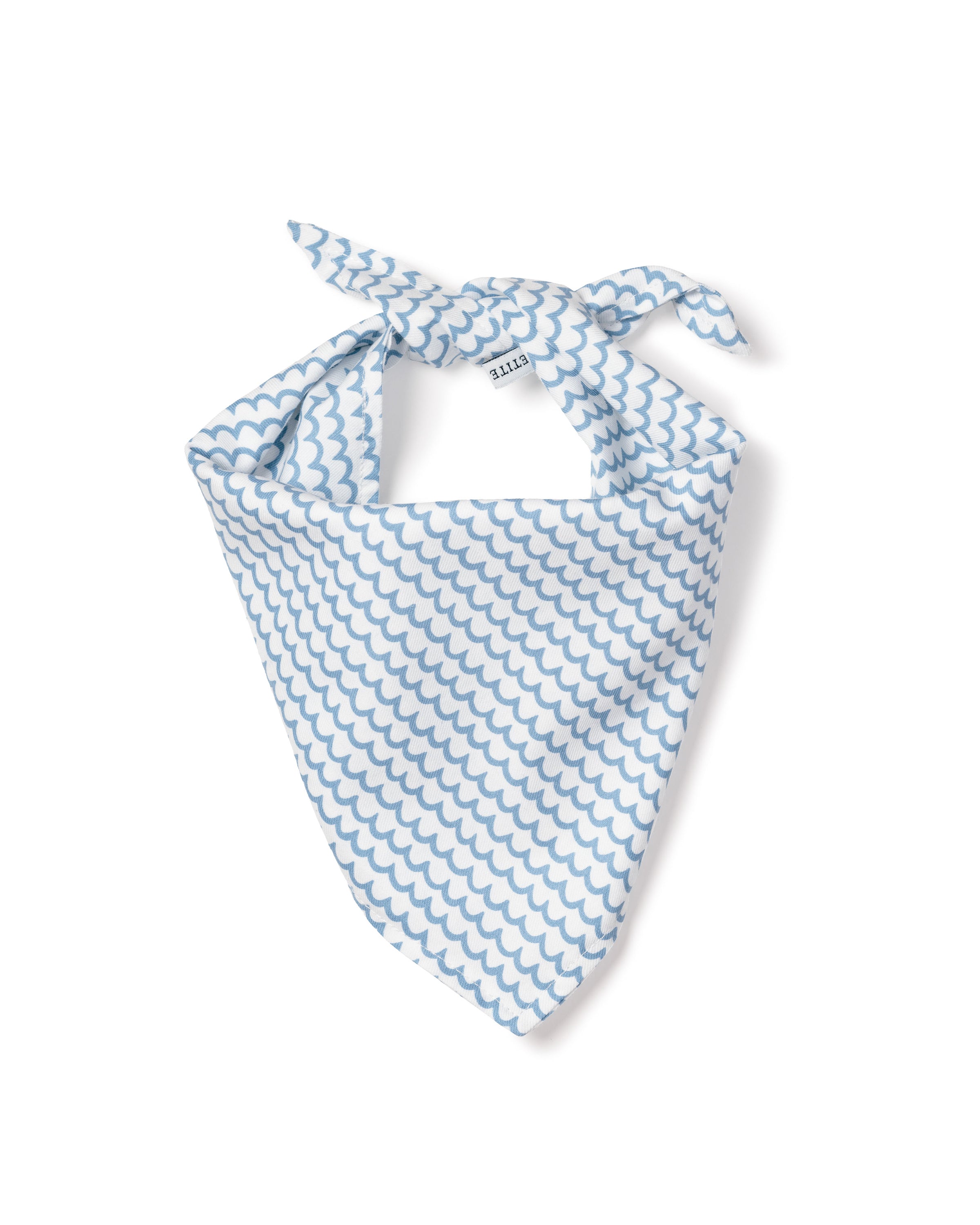 A fluffy white dog sits on a wooden floor, wearing the charming Petite Plume Dog Bandana in La Mer made from blue and white checkered fabric. The dog looks up happily with its tongue slightly out, highlighting the latest in stylish dog accessories.