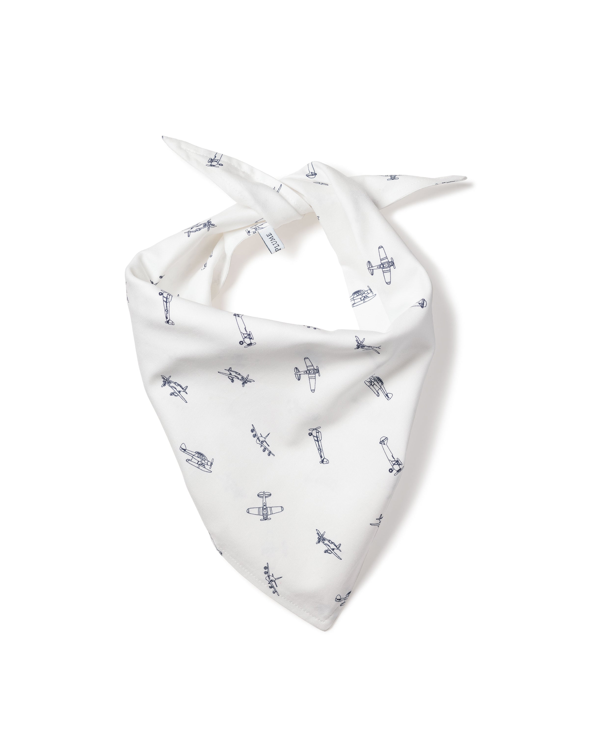 A fluffy white dog with small ears wears the Petite Plume Par Avion Dog Bandana featuring a blue floral pattern. The happy pup lies on a light wooden floor, looking up with its mouth open, showcasing the perfect blend of style and comfort in dog accessories.