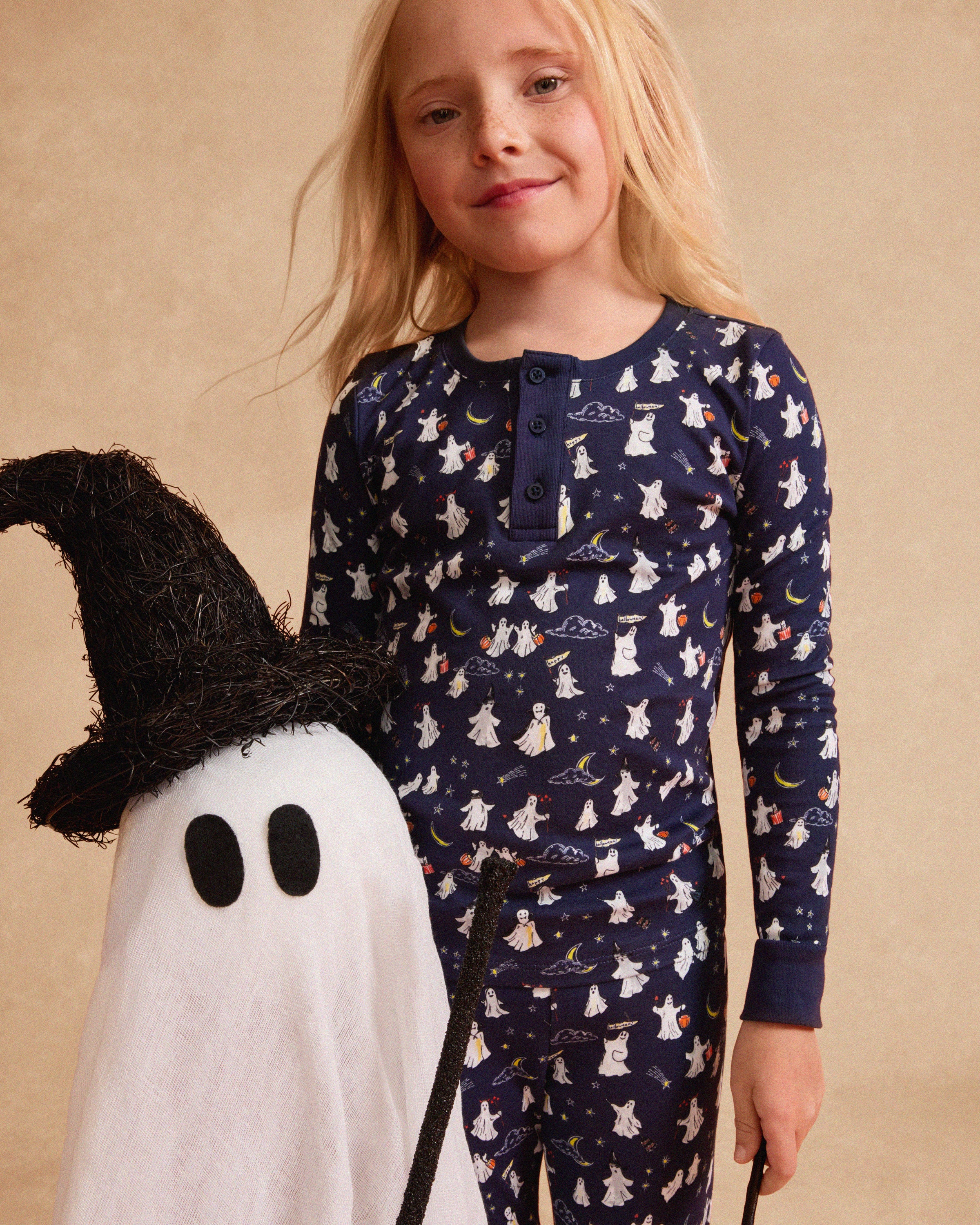 The Kid's Pima Snug Fit Pajama Set in Spooky Slumber is a navy blue pajama set with long sleeves and pants, featuring white and red cartoon dogs in winter gear, plus dark blue cuffs and button details on the top.