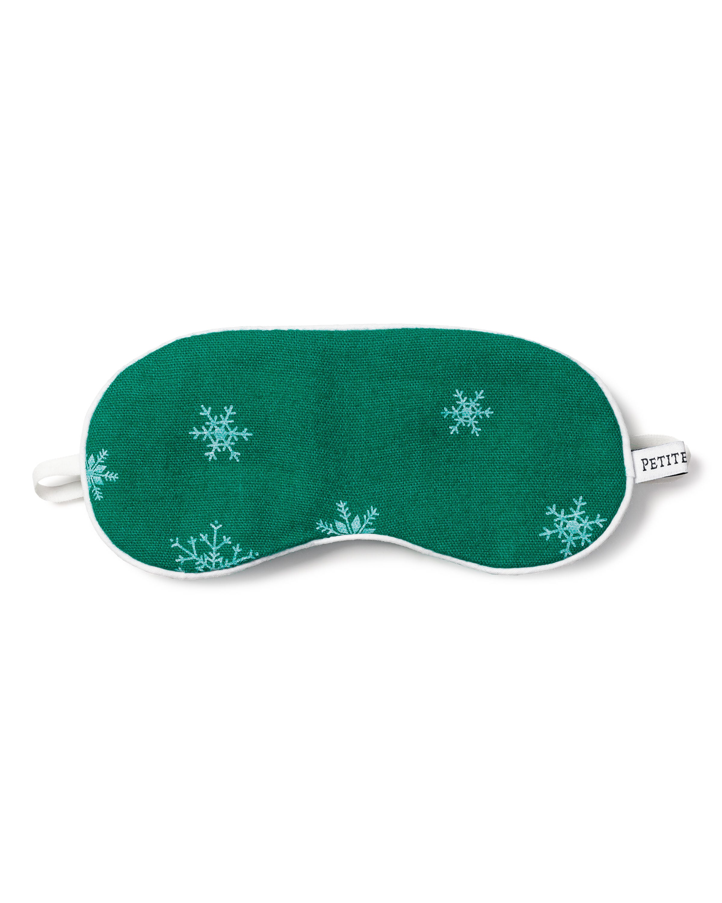 The Kids Flannel Sleep Mask in Emerald Wonderland by Petite Plume is emerald green with white snowflake patterns, a white border, and features an elastic strap. A small tag on the side reads PETITE.