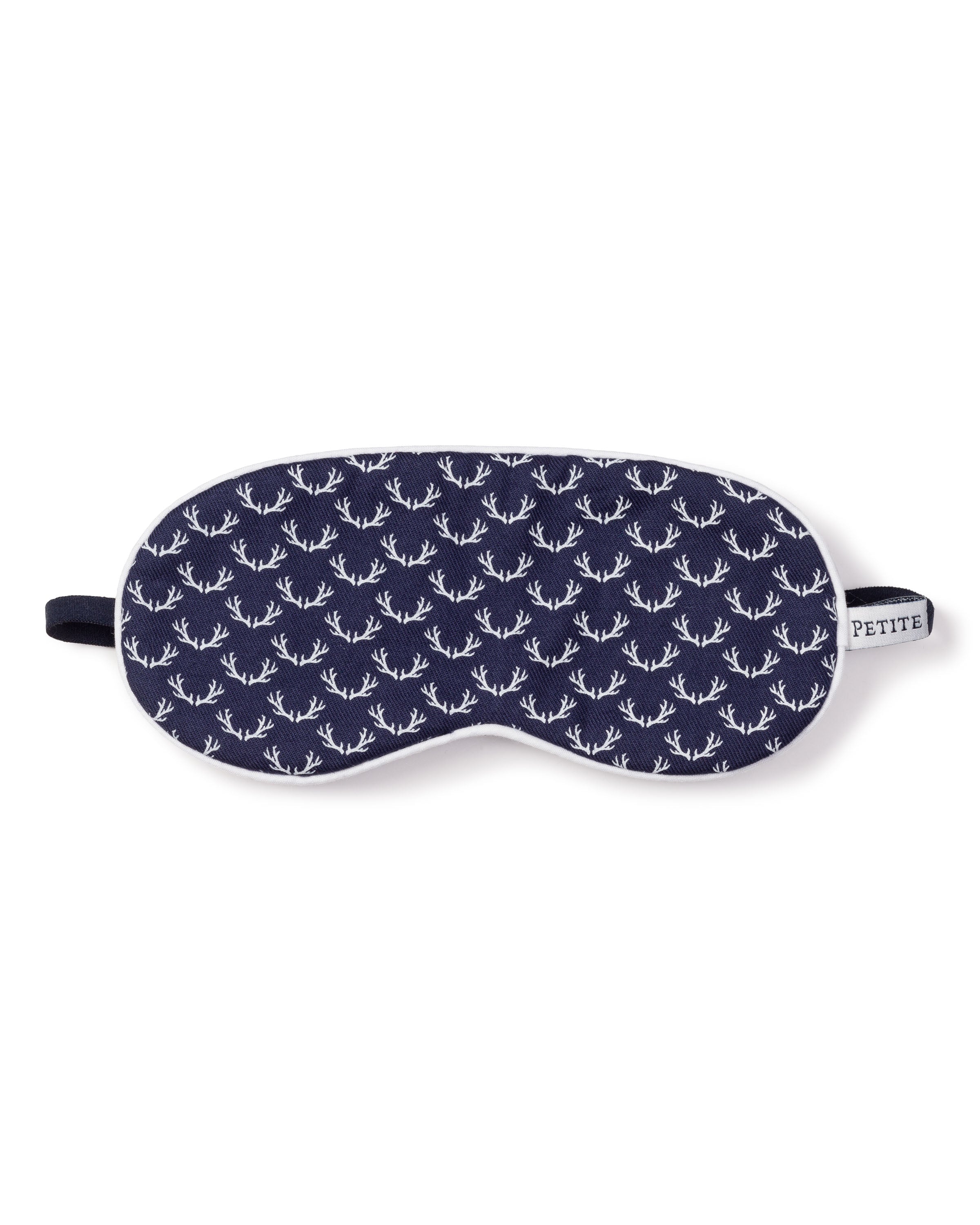 The Kids Twill Sleep Mask in Nordic Antlers by Petite Plume features a navy blue design with white antlers, a black elastic strap, and a PETITE fabric tag, ideal for matching with luxurious sleepwear.
