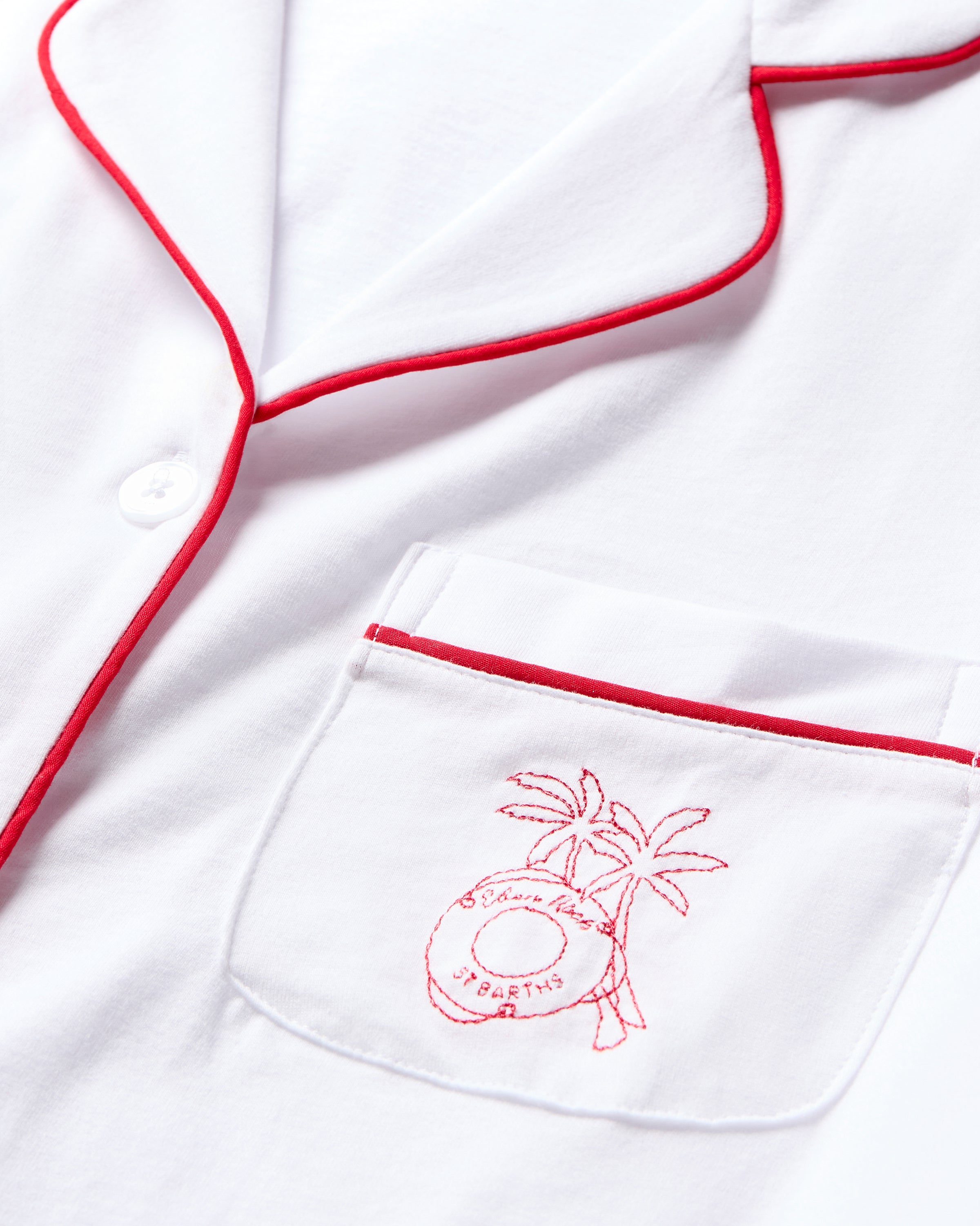Close-up of the Petite Plume x Eden Rock St Barth Womens White Pima Pajama Set, featuring a chest pocket with red piping and embroidery of a palm tree and life preserver. The limited-edition evokes Caribbean paradise with soft, luxurious fabric and Ocean Club Yachting design.