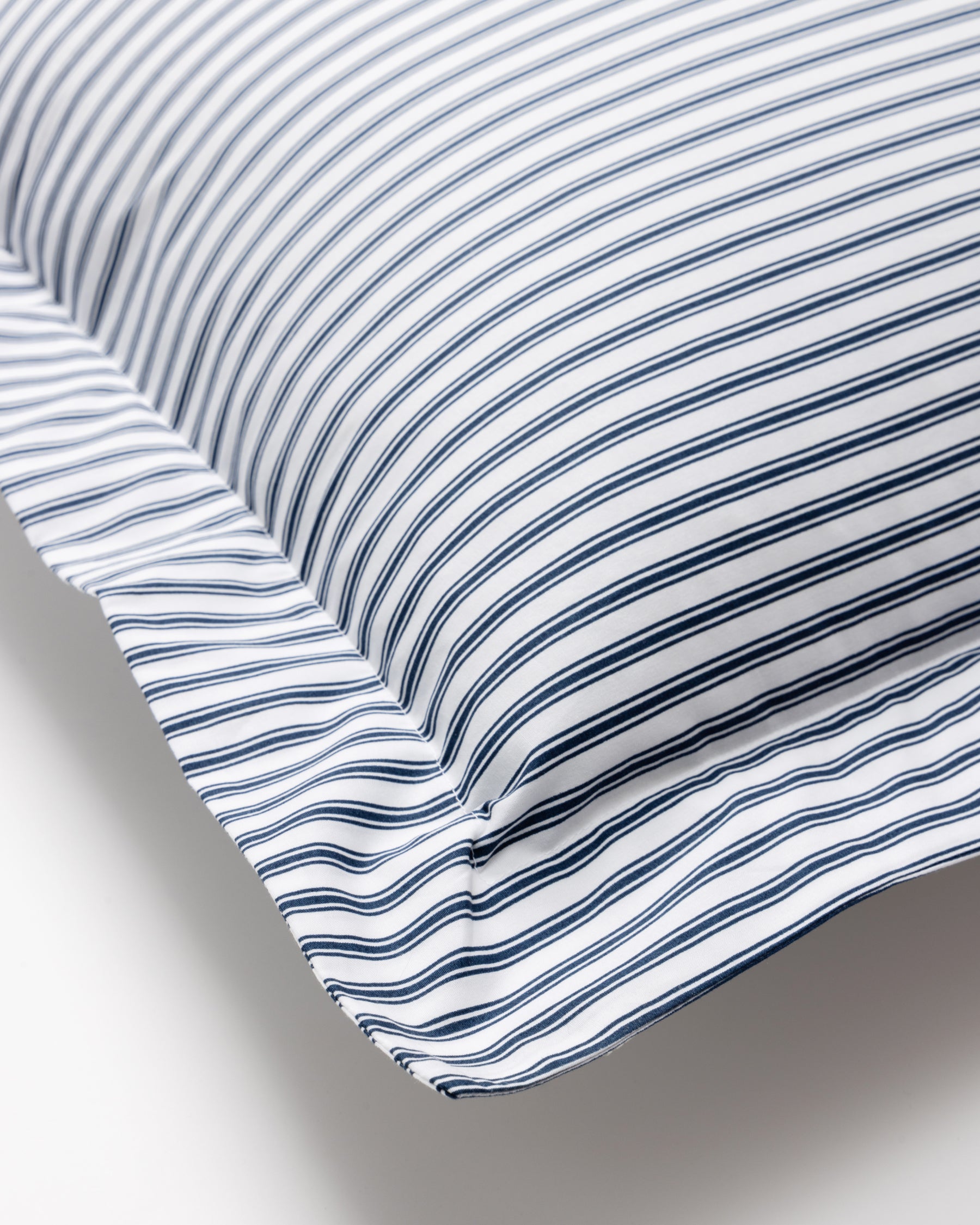 The Luxe Premium Cotton Euro Sham in Navy French Ticking by Petite Plume features thin, evenly spaced blue and white stripes. Its clean look enhances the smooth percale fabric texture and neat edge stitching, combining elegance with comfort.
