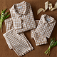 Two sets of matching brown and white checkered pajamas, neatly folded, displayed on a brown surface with green sprigs and beige ribbon for decoration.