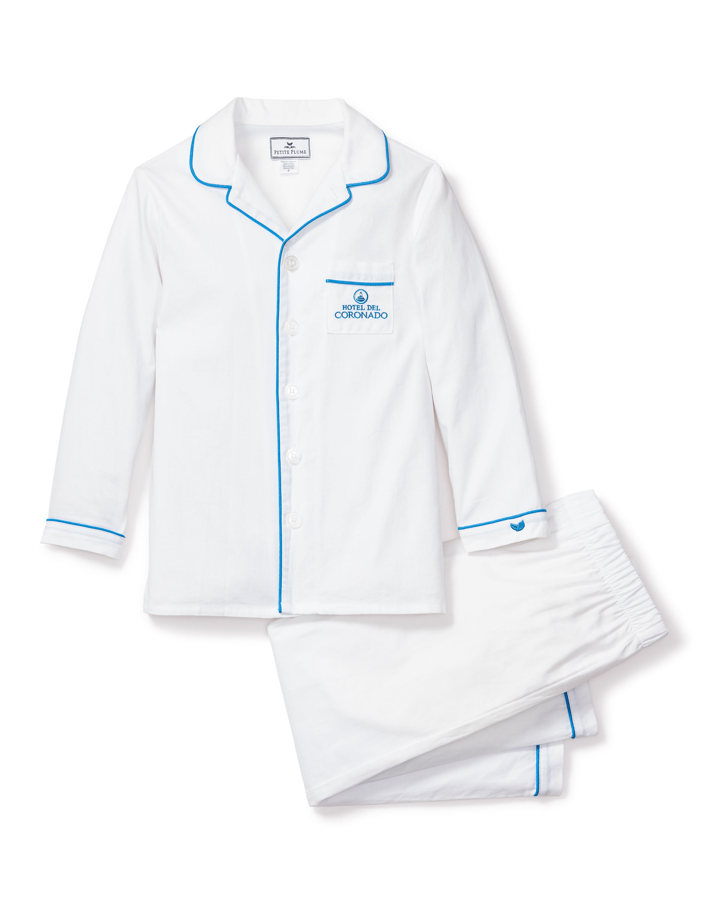 This elegant Kids Twill Pajama Set by Petite Plume features white cotton fabric with blue piping. It includes a long-sleeve, button-up shirt adorned with a Coronado Beach logo and matching pants with an elastic waistband.