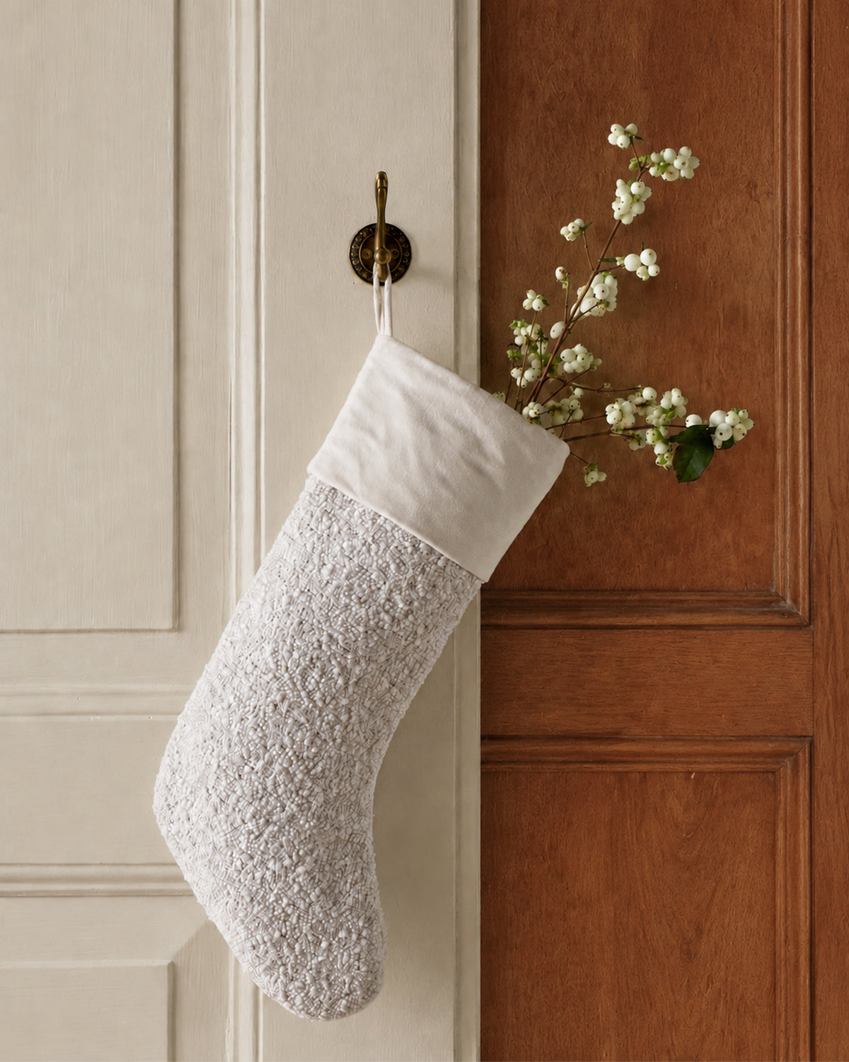 Cream-colored textured Boucle Christmas Stocking in Cream hanging on a hook, filled with sprigs of white berries.