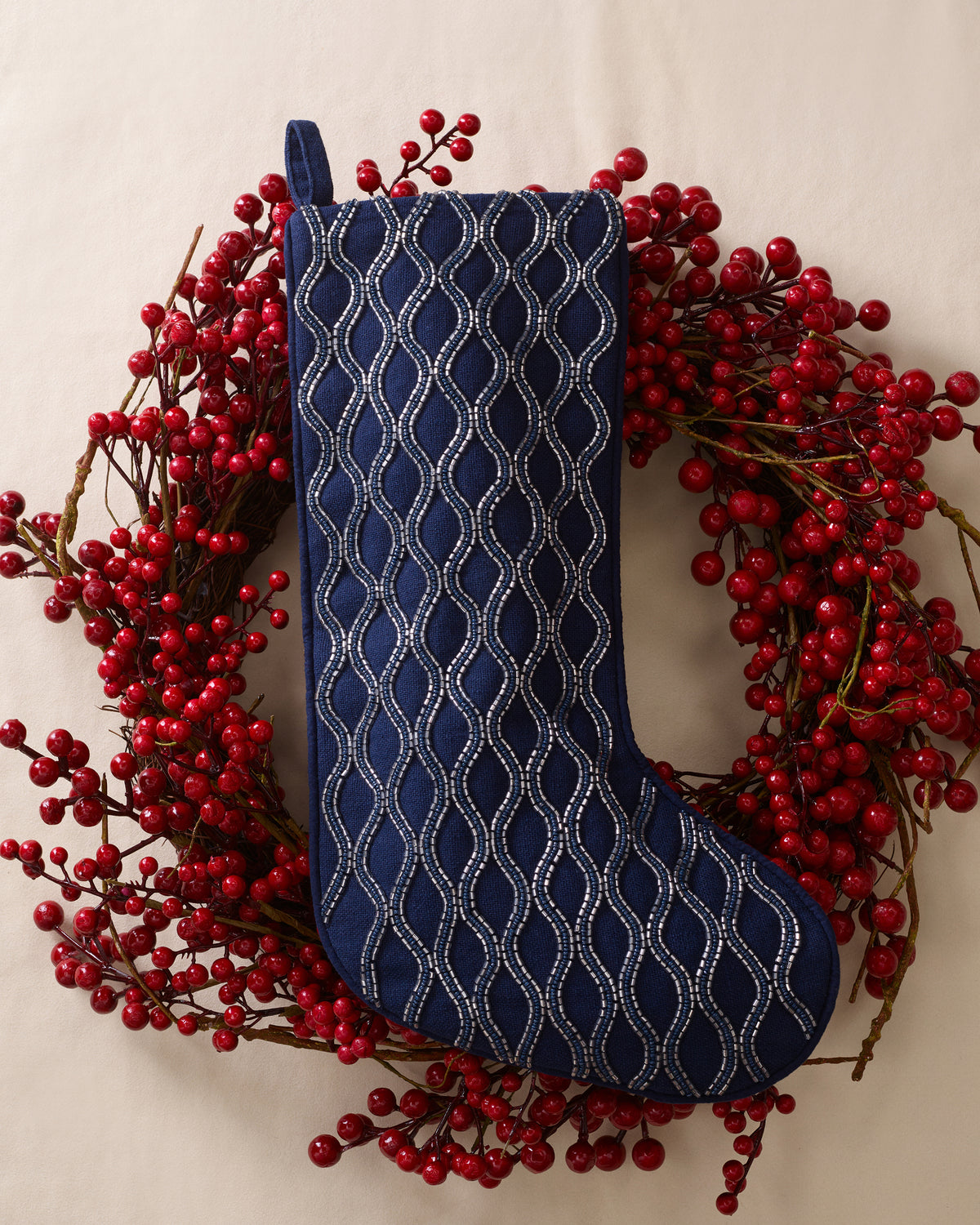 Beaded Christmas Stocking in Navy with a silver beaded wavy pattern, hanging over a wreath of red berries.