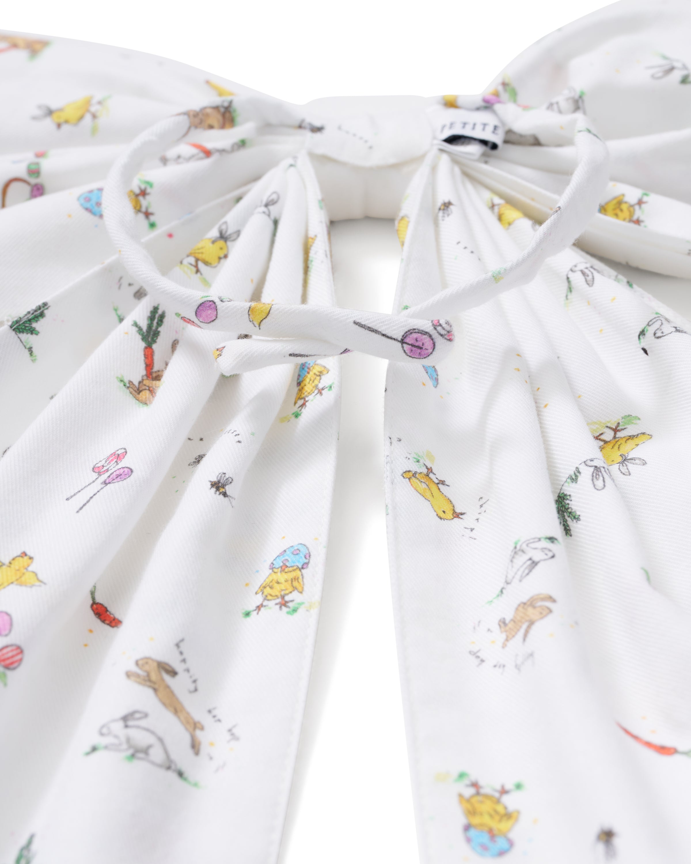 An Easter Basket and Wreath Bow in Easter Frolic with a large white bow featuring a pastel floral pattern is tied at the bottom of a wreath made of small white and pink flowers, hanging on a beige door.