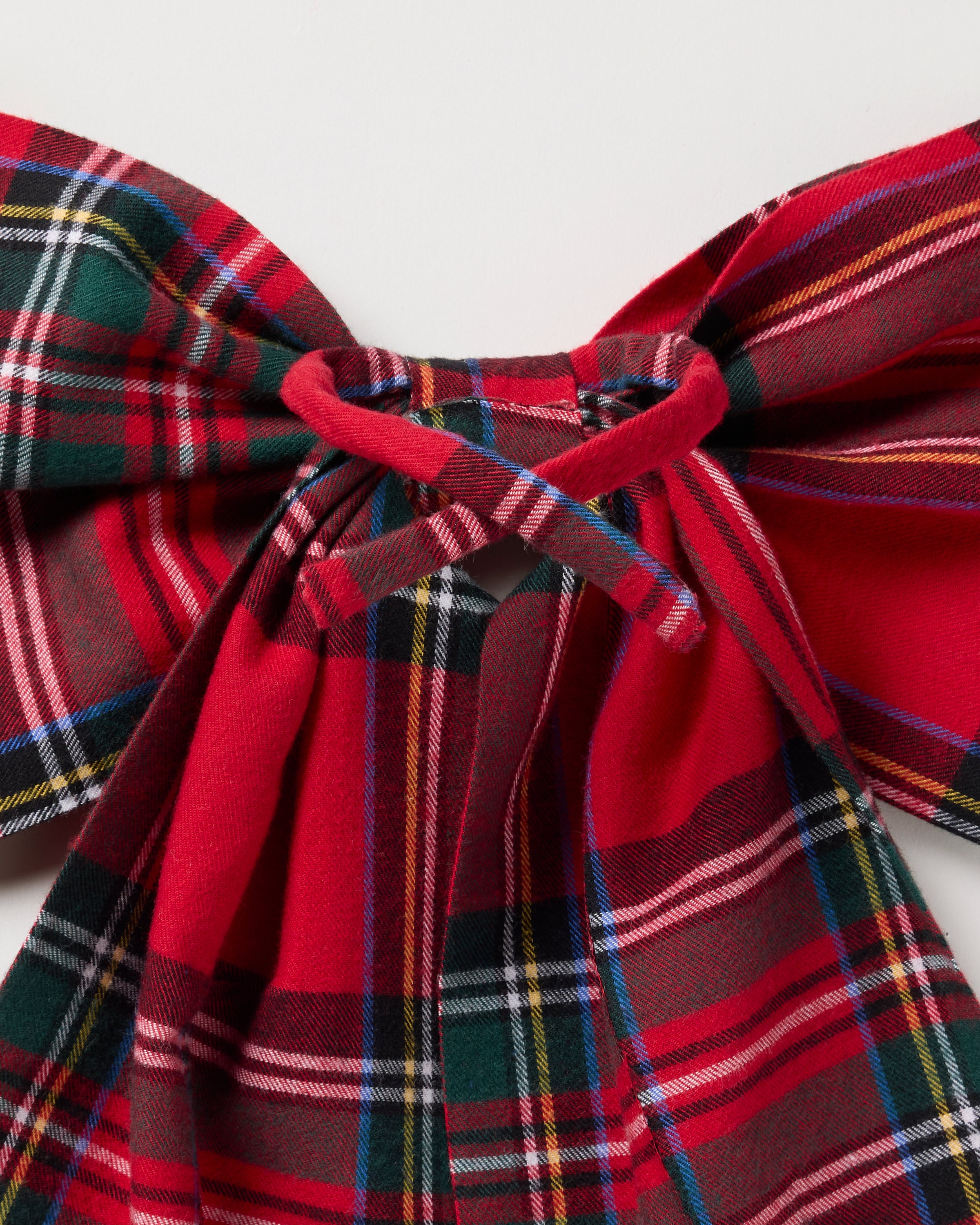 Close-up of Petite Plumes Wreath Bow in Imperial Tartan, ideal for holiday decor or sleepwear embellishment. The red plaid fabric showcases green, blue, yellow, and white lines with symmetrical loops and tails on a plain white background.