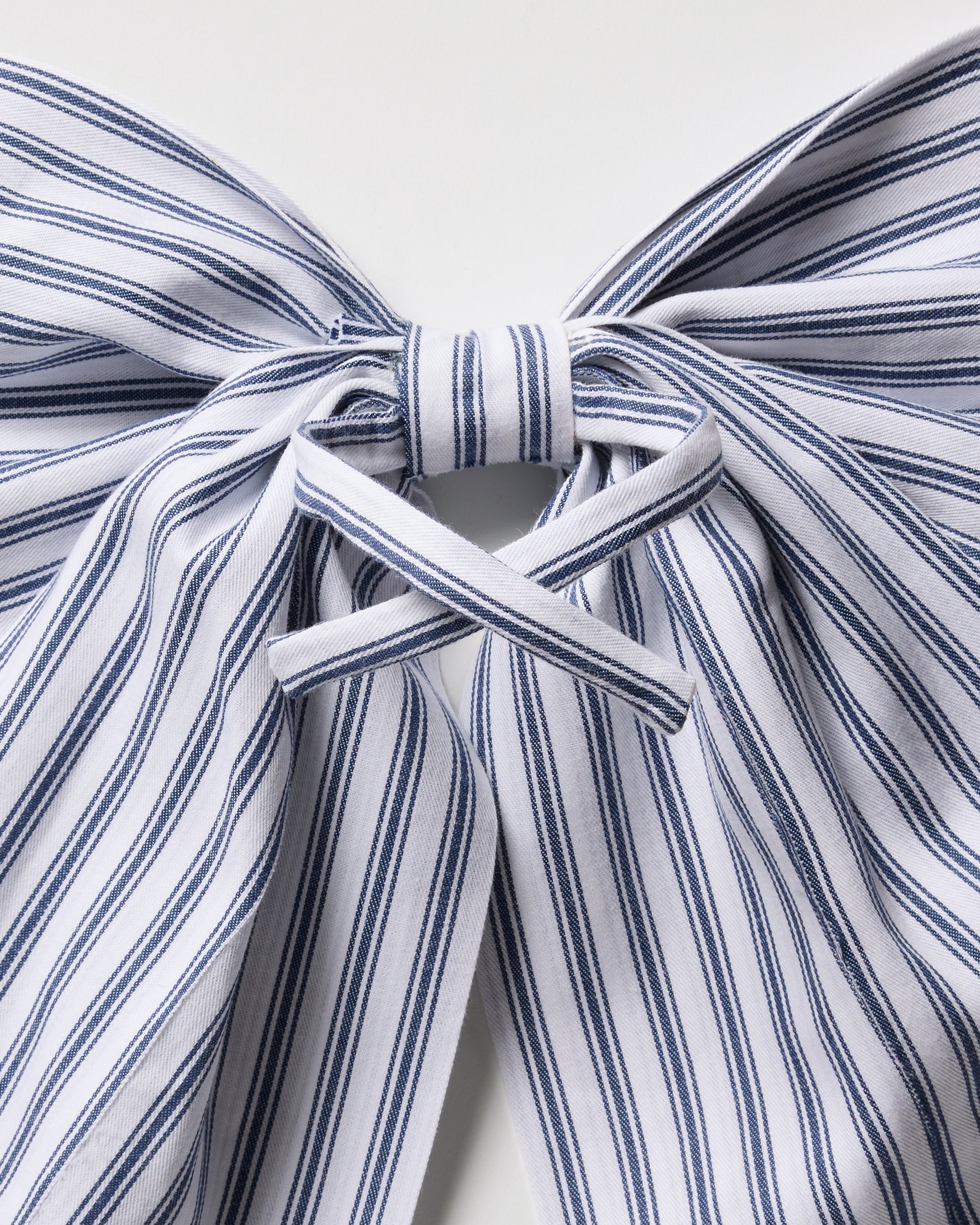 The Wreath Bow in Navy French Ticking by Petite Plume features a large, neatly tied fabric bow with blue and white vertical stripes on a white background, offering a classic, elegant look ideal for enhancing your holiday decor.
