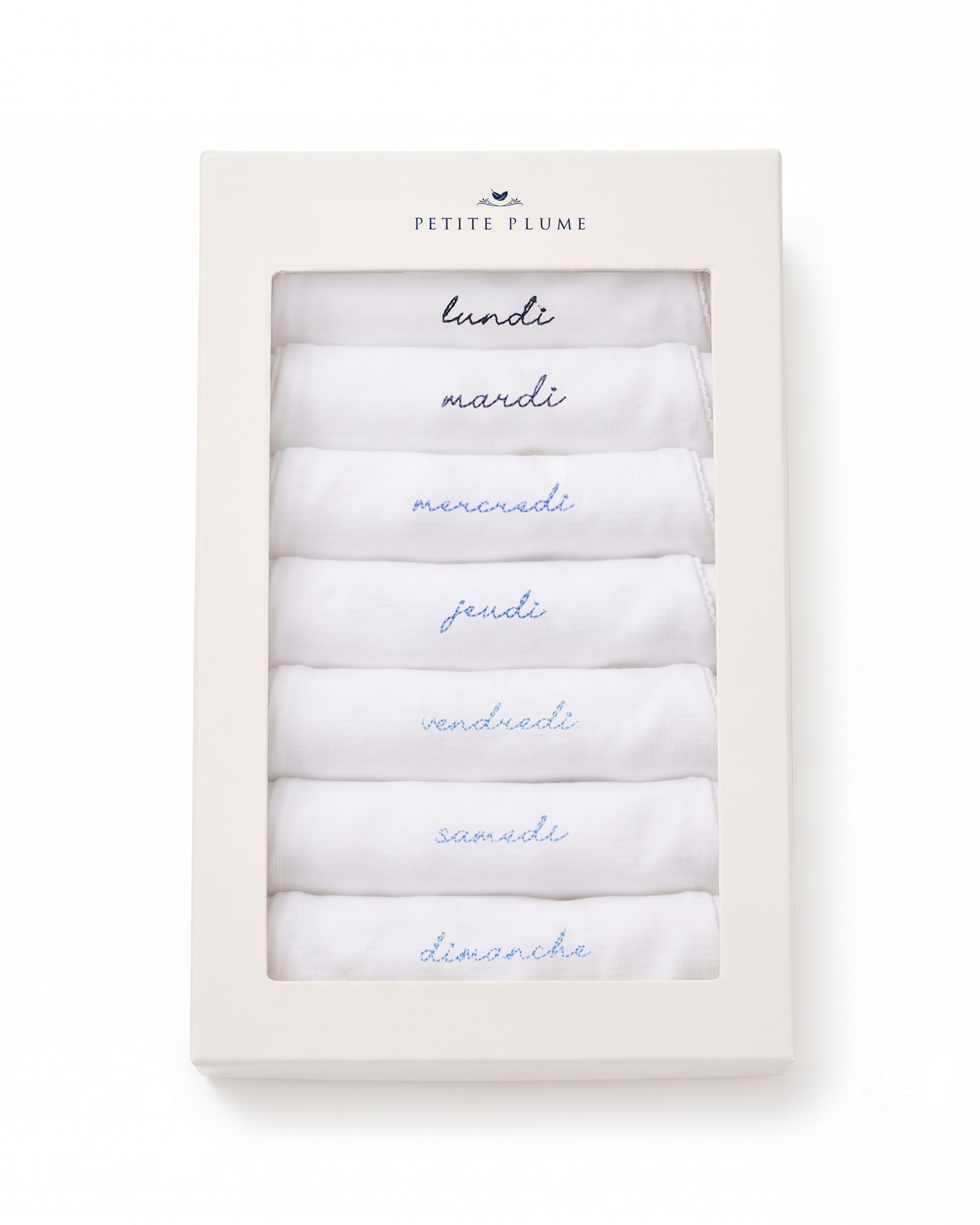 A box labeled “Baby’s Pima Long Sleeve Onesie Set in French Lessons Blue” contains seven folded white onesies, each embroidered with the days of the week in French: lundi, mardi, mercredi, jeudi, vendredi, samedi, and dimanche.