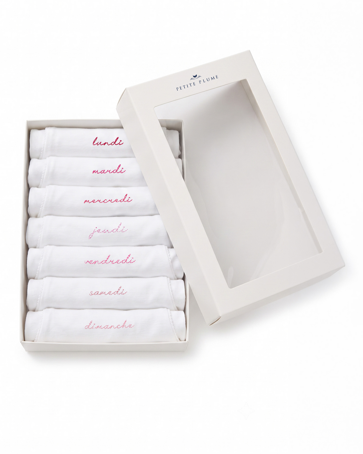 Set of seven Baby’s Pima Short Sleeve Onesies in French Lessons Pink, each embroidered with a day of the week in French, neatly displayed in a white box with a clear lid.
