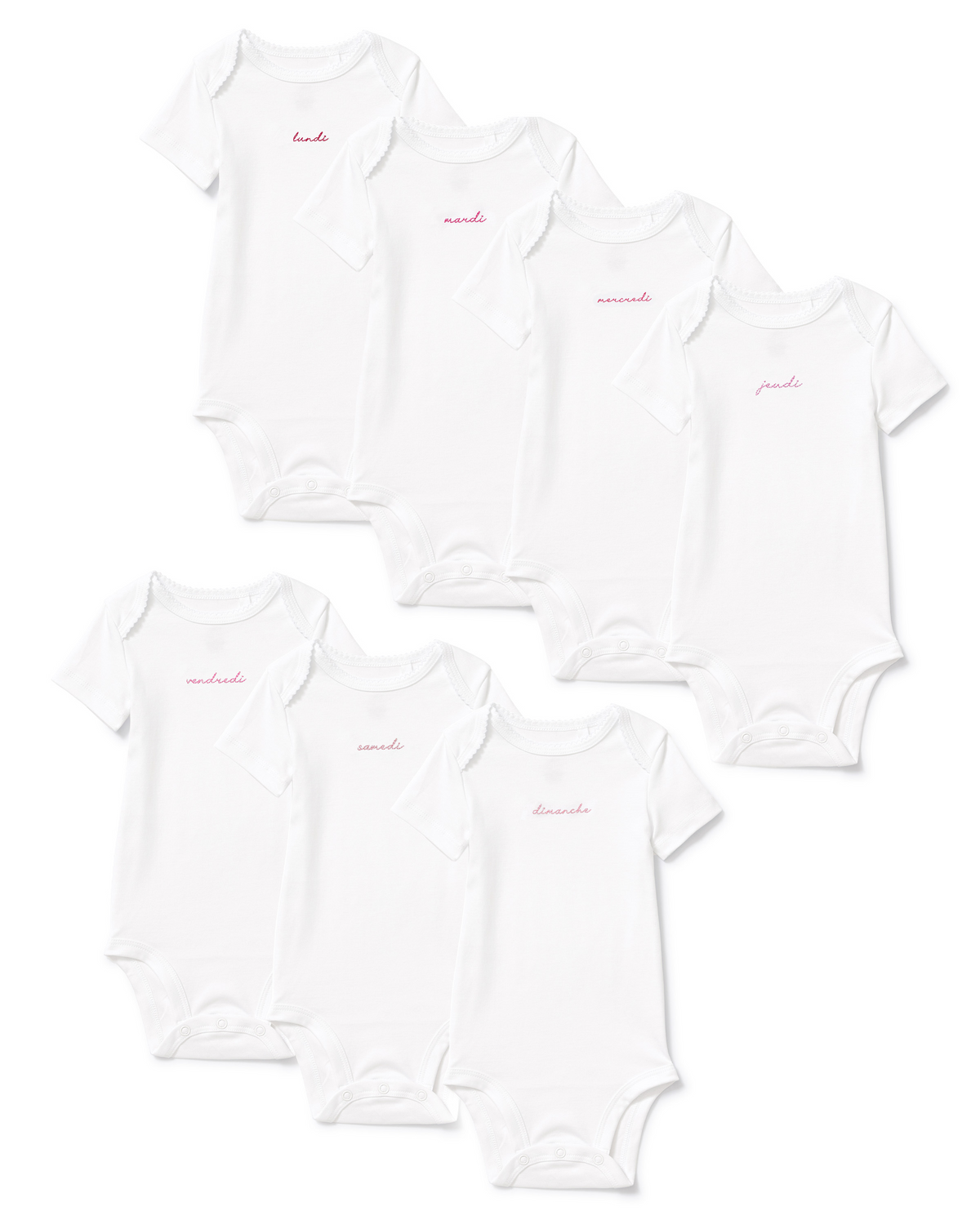Seven white Baby’s Pima Short Sleeve Onesies from the French Lessons Pink set are arranged in two rows. Each onesie features a different day of the week written in pink cursive Spanish on the chest.