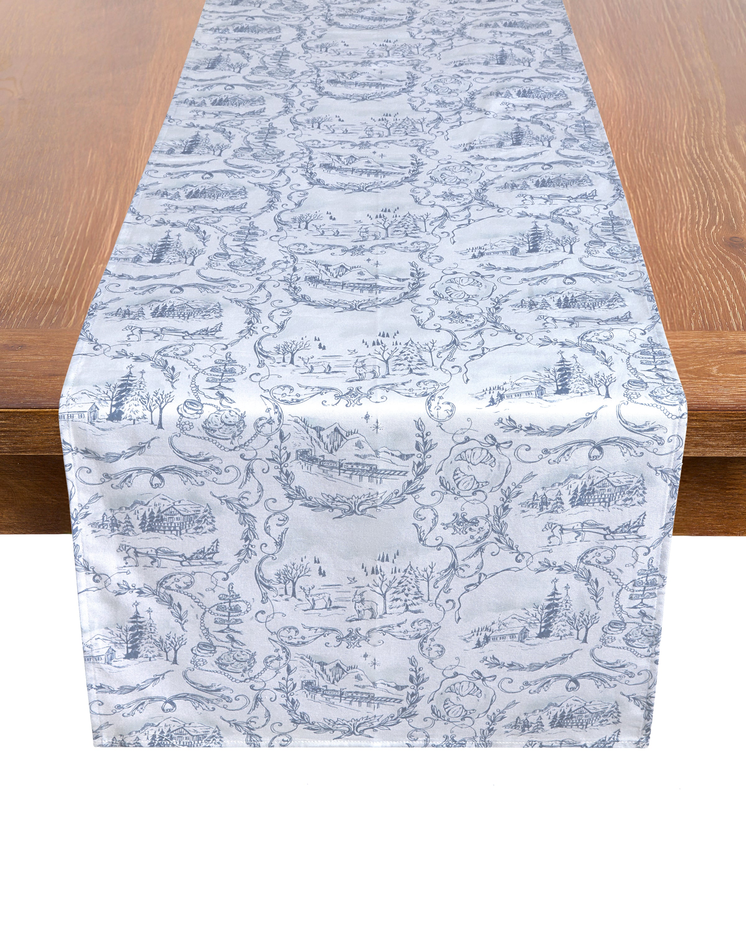 The Maman x Petite Plume Alpine Toile Runner by Petite Plume is a wooden table accent crafted from 100% cotton, featuring slate blue pastoral motifs of landscapes, trees, and rustic scenes to create an elegant and serene festive ambiance.