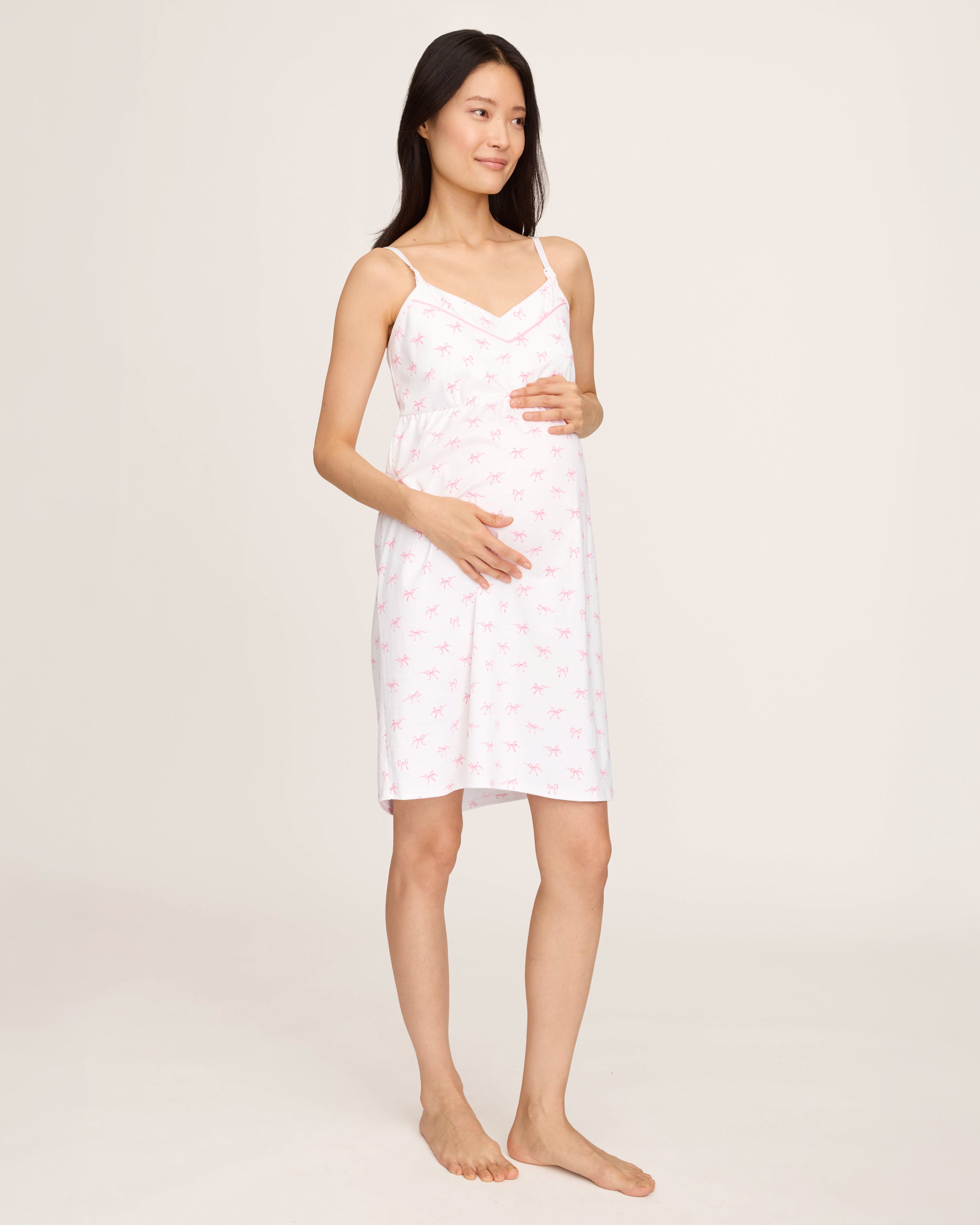 The Women's Pima Maternity Nightgown in Blushing Bows is a white sleeveless spaghetti strap dress with a fitted bust, slightly flared skirt, and an all-over print of small pink bows.