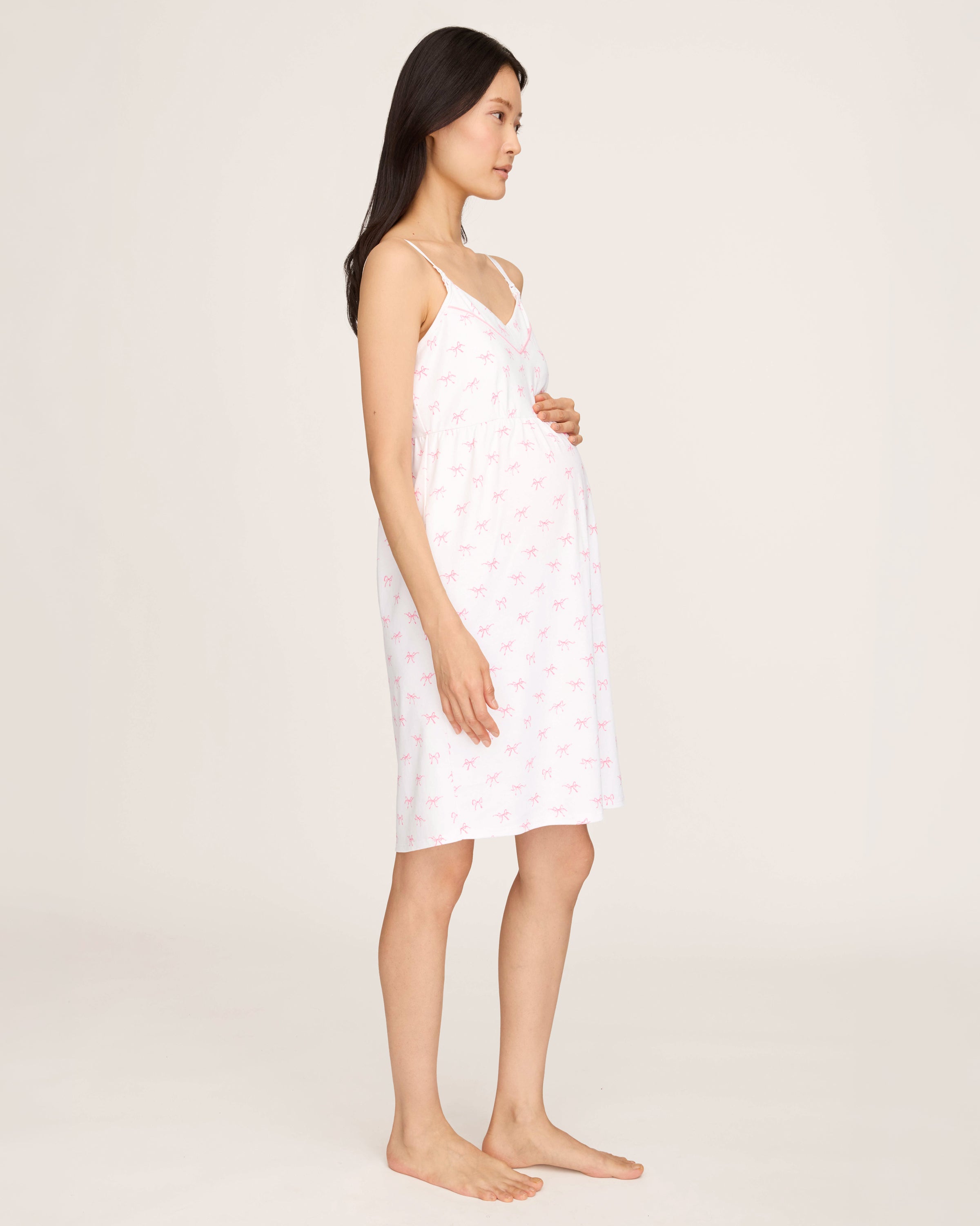 The Women's Pima Maternity Nightgown in Blushing Bows is a white sleeveless spaghetti strap dress with a fitted bust, slightly flared skirt, and an all-over print of small pink bows.