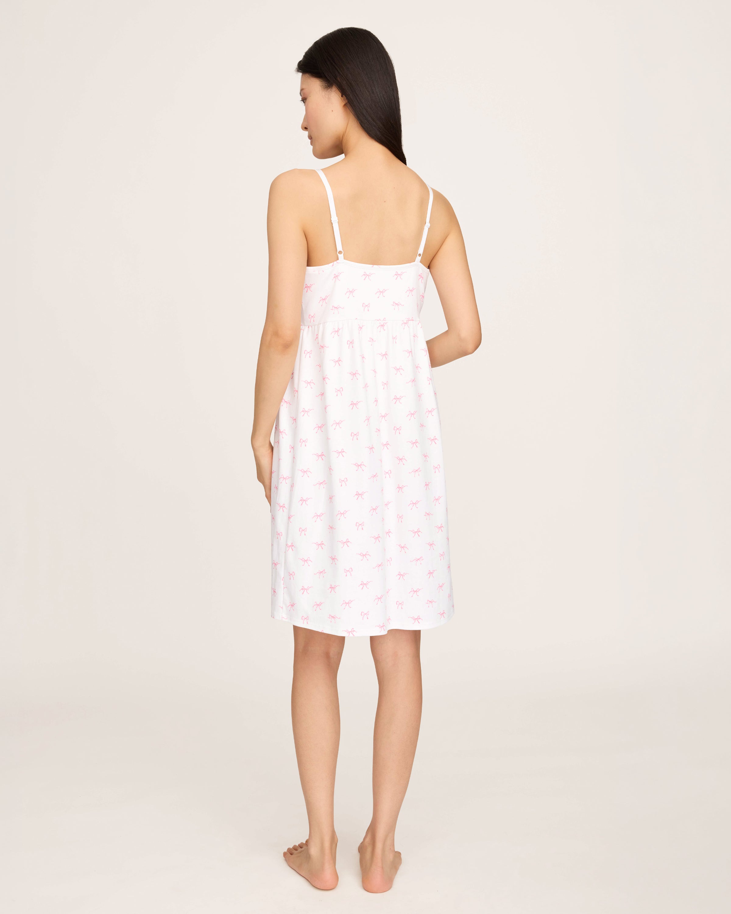 The Women's Pima Maternity Nightgown in Blushing Bows is a white sleeveless spaghetti strap dress with a fitted bust, slightly flared skirt, and an all-over print of small pink bows.