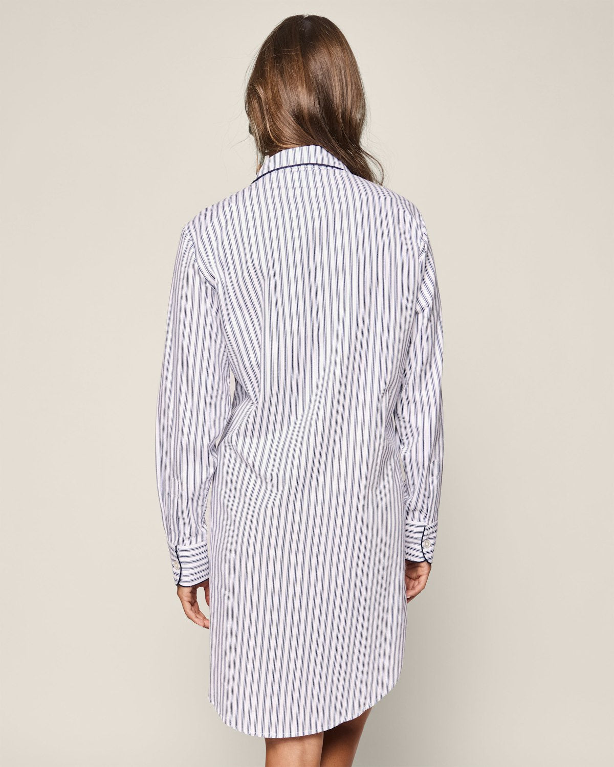 A person with long hair wears the Petite Plume Womens Twill Maternity Nightshirt in Navy French Ticking, shown from the back. The premium cotton enhances its collar and buttoned cuffs, while a plain background highlights this stylish shirtdress.