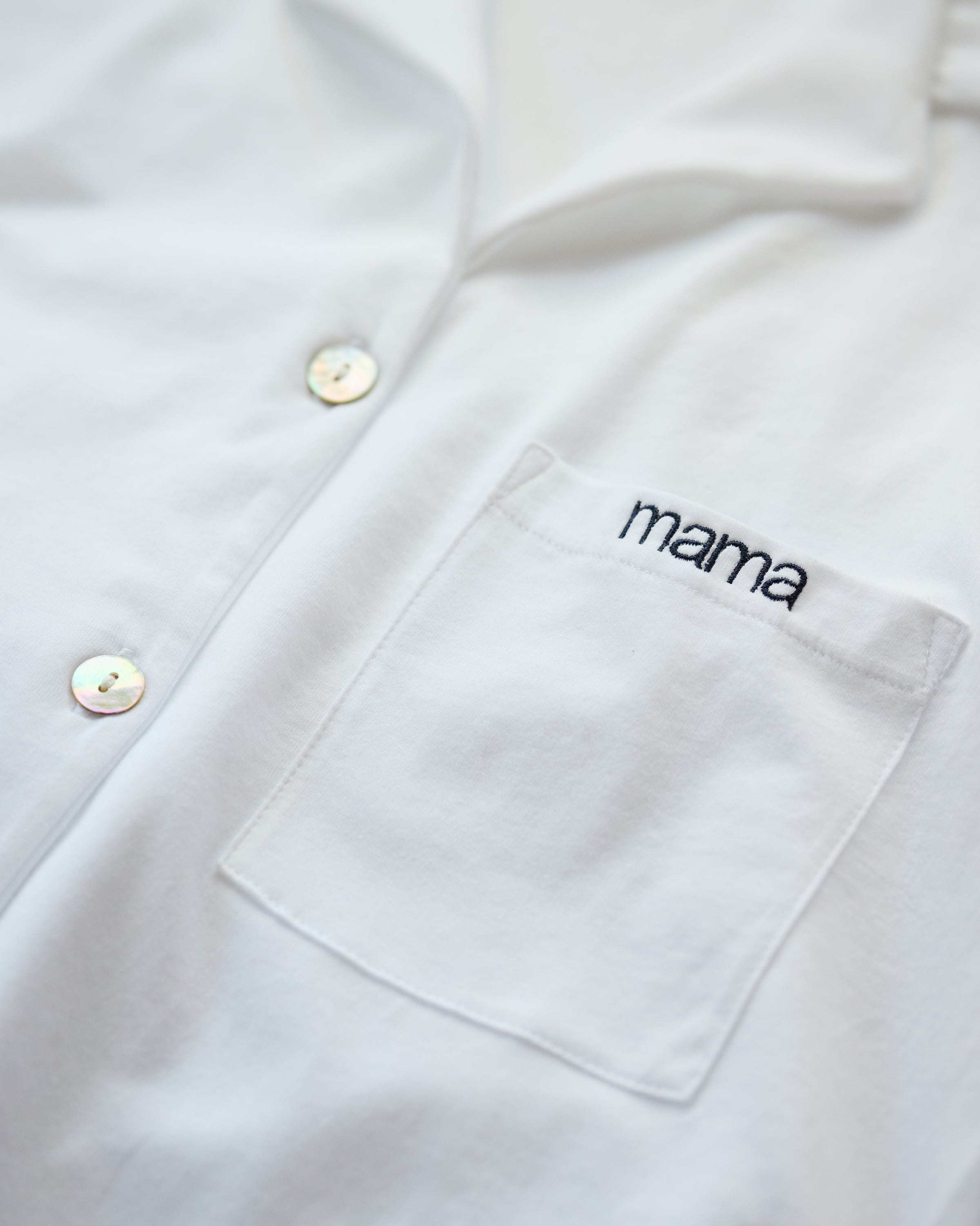 Close-up of The Olivia Wide Leg Pima Pajama Set by Petite Plume, showcasing the white button-up shirt with mama embroidered above a pocket. Featuring pearly buttons and simple design, its an ideal Mothers Day gift.