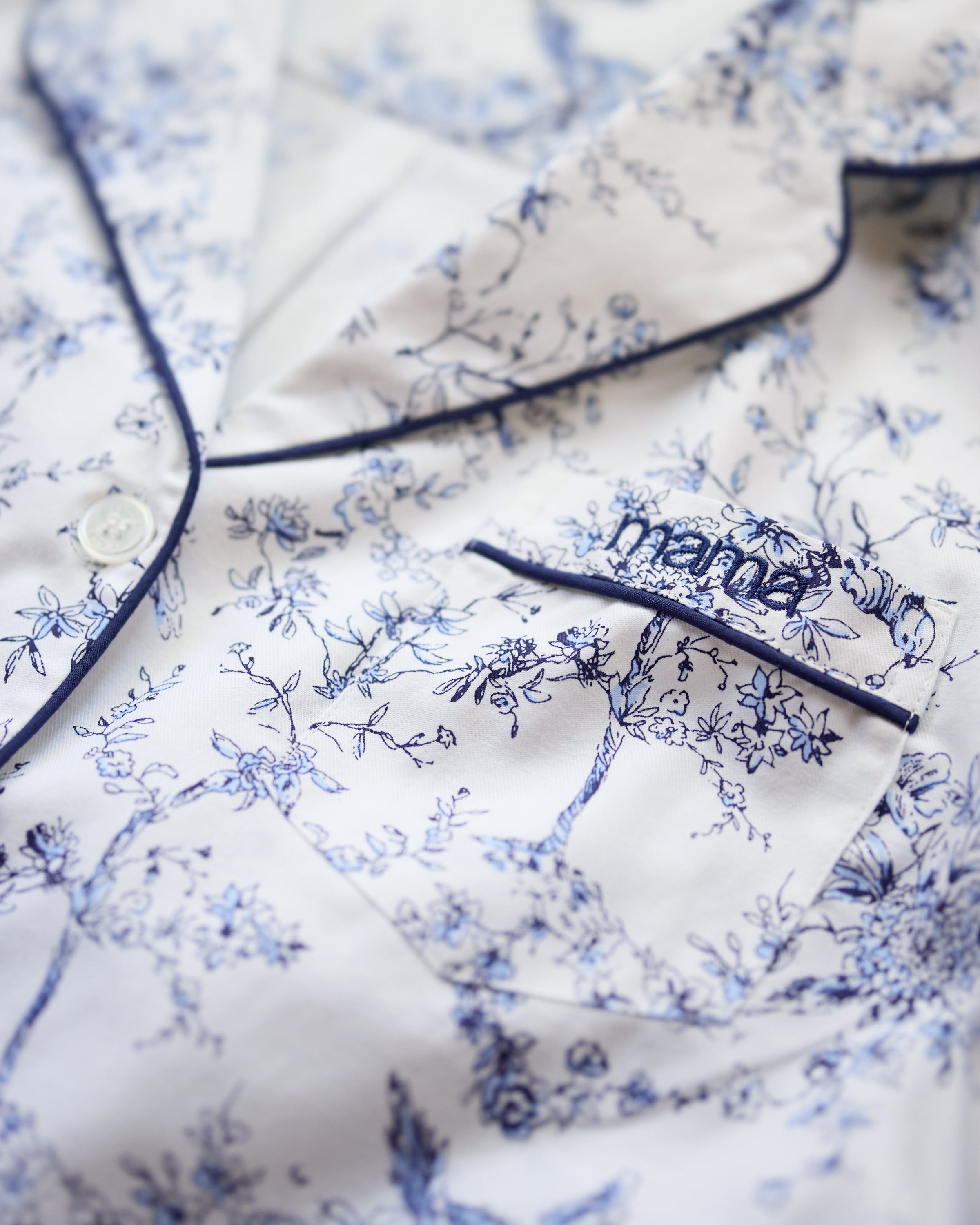Luxurious close-up of a Petite Plume Womens Pima Pajama top featuring timeless toile botanical flowers in blue with dark blue piping and buttons. The pocket showcases Mama embroidery, making it a perfect Mothers Day gift.