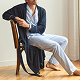 A person wearing light blue pajamas and a dark blue robe sits barefoot on a wooden chair in a sunlit room with wooden floors.