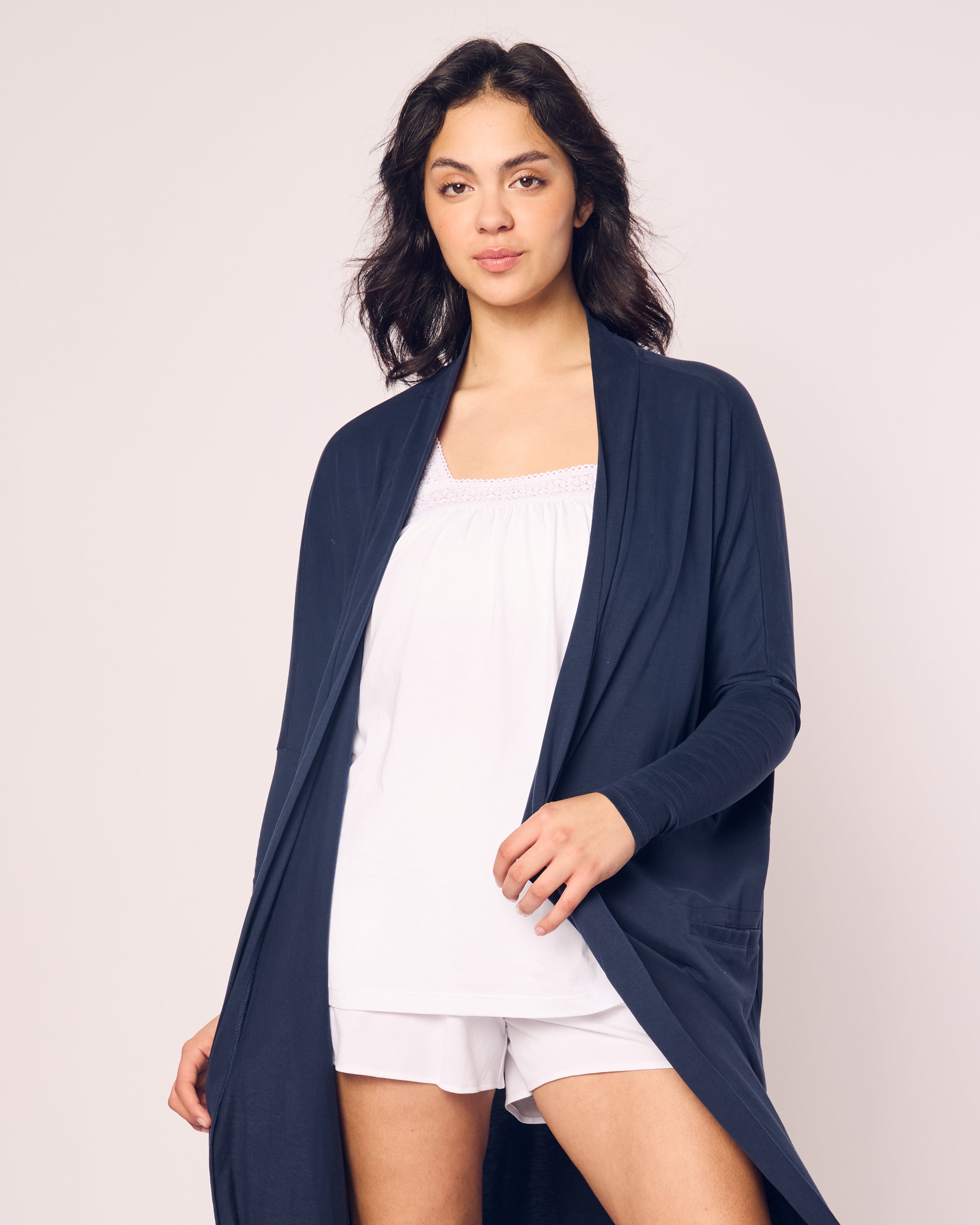 A person with long dark hair stands against a plain background, wearing a white top and shorts made from breathable fabric, paired with Petite Plumes Womens Pima Duster in Navy.