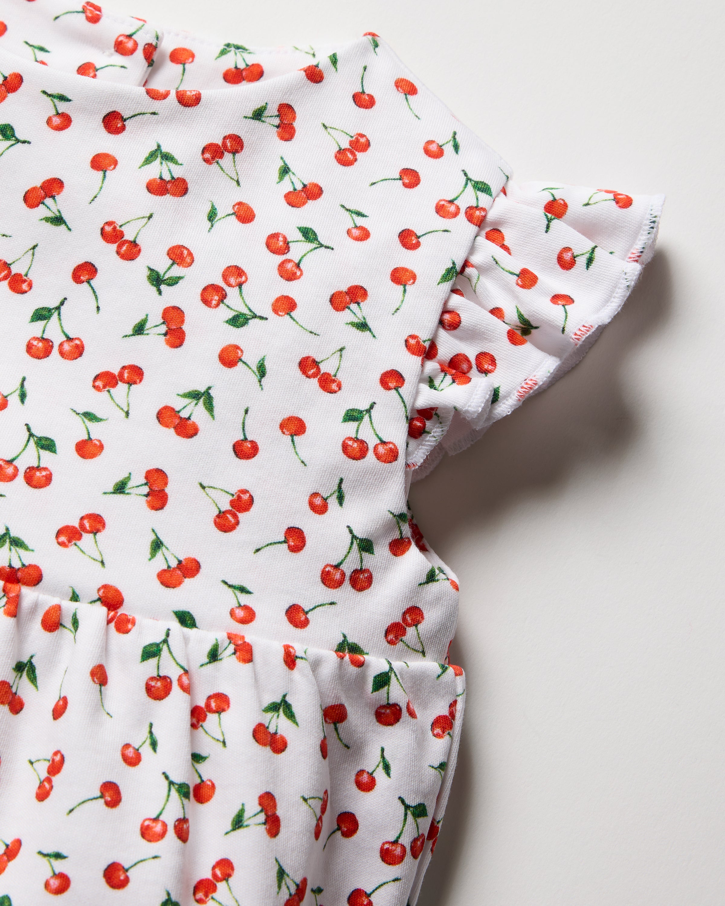 The Babys Pima Isla Play Romper in Cherry Orchard by Petite Plume features a delicate red cherry print on soft Pima cotton, complete with gathered short sleeves and a ruched waist—perfect for playful mom-and-me summer outfits or as an adorable childs garment.