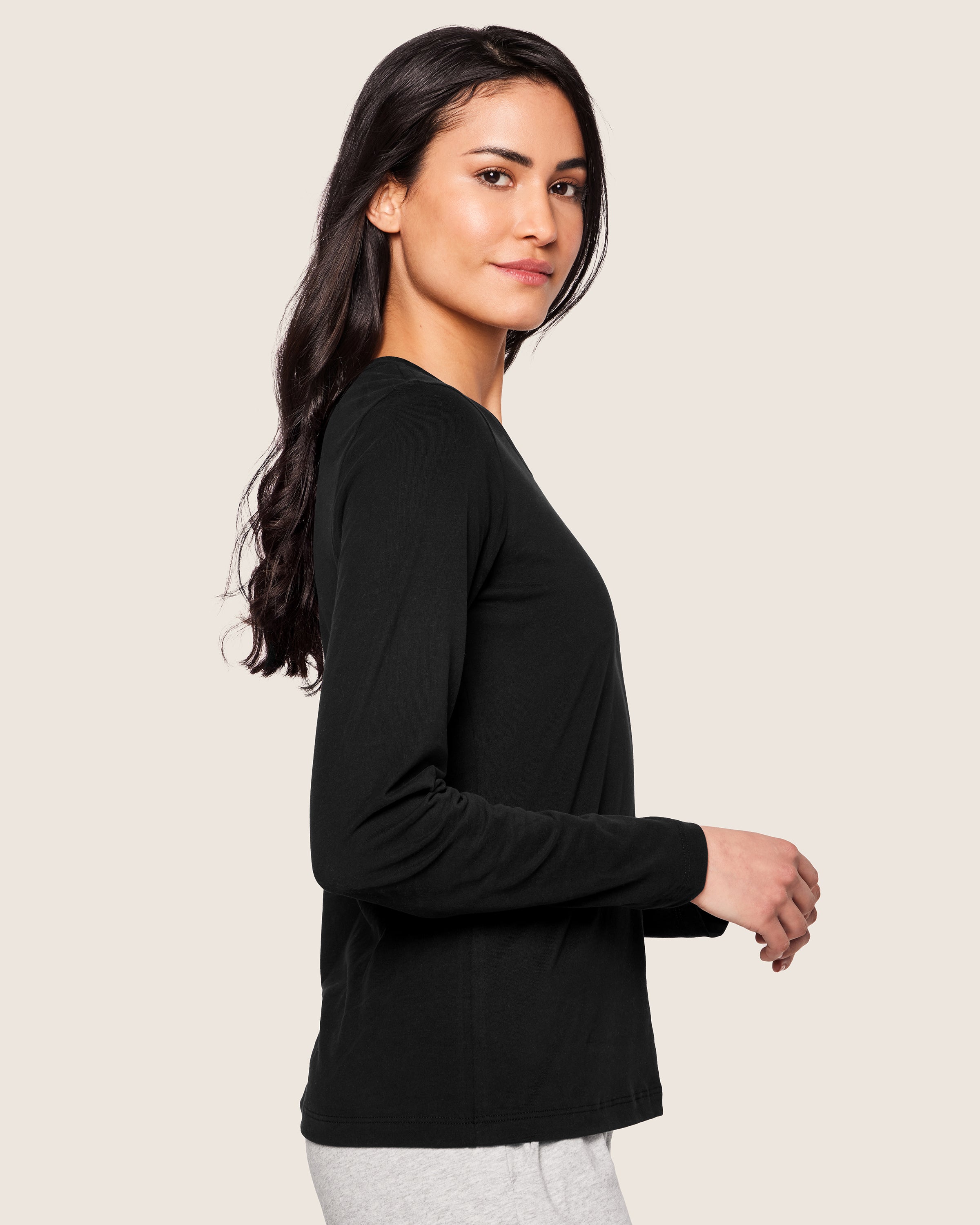 A person with long dark hair models a tailored Petite Plume Womens Pima Long Sleeve Top in Black, paired with light gray Pima Cotton pants, standing sideways on a plain background.