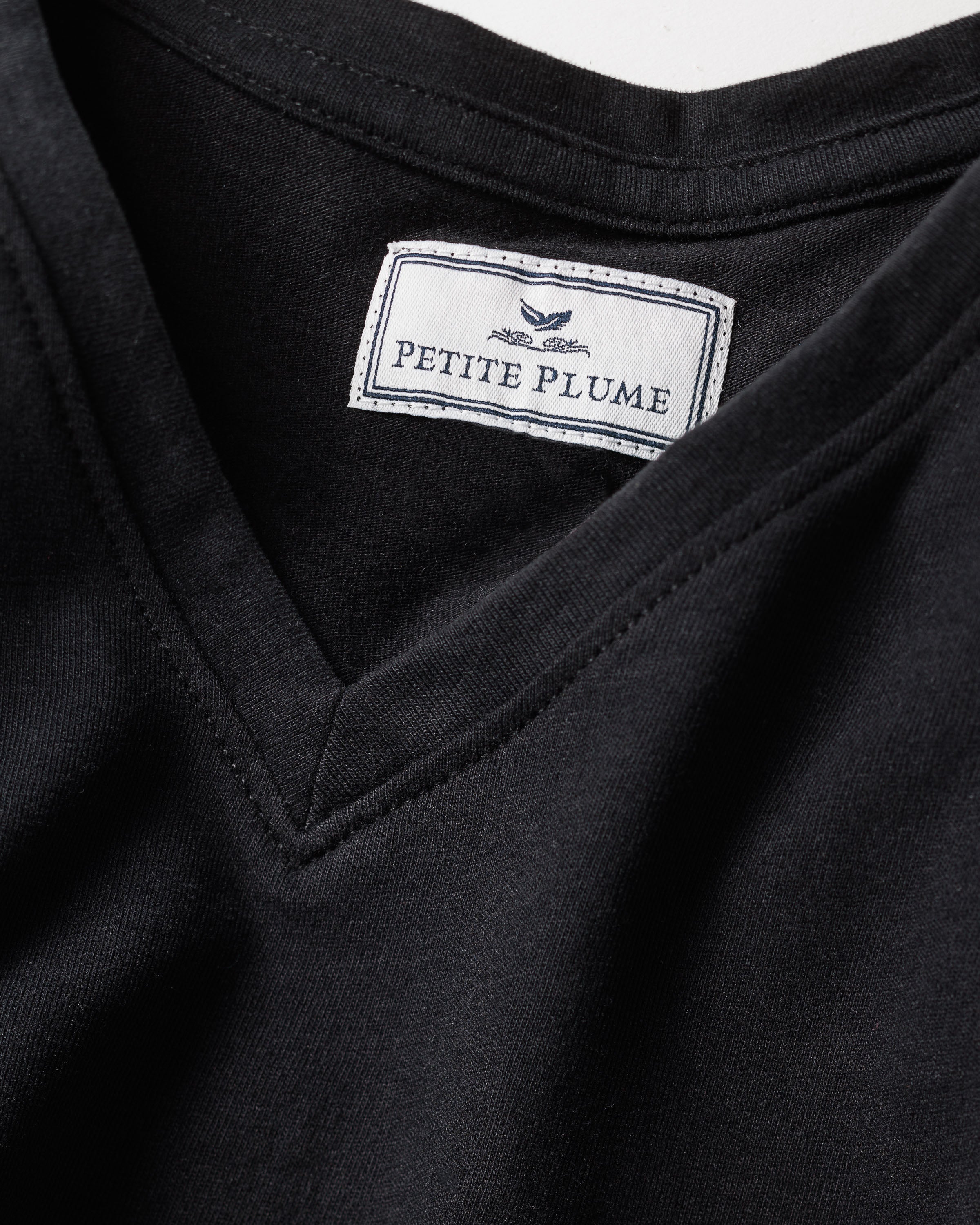 Close-up of the Womens Pima Short Sleeve Top in Black by Petite Plume, crafted from soft Peruvian Pima cotton. The neckline label features Petite Plume with a feather graphic, symbolizing luxury elegance.
