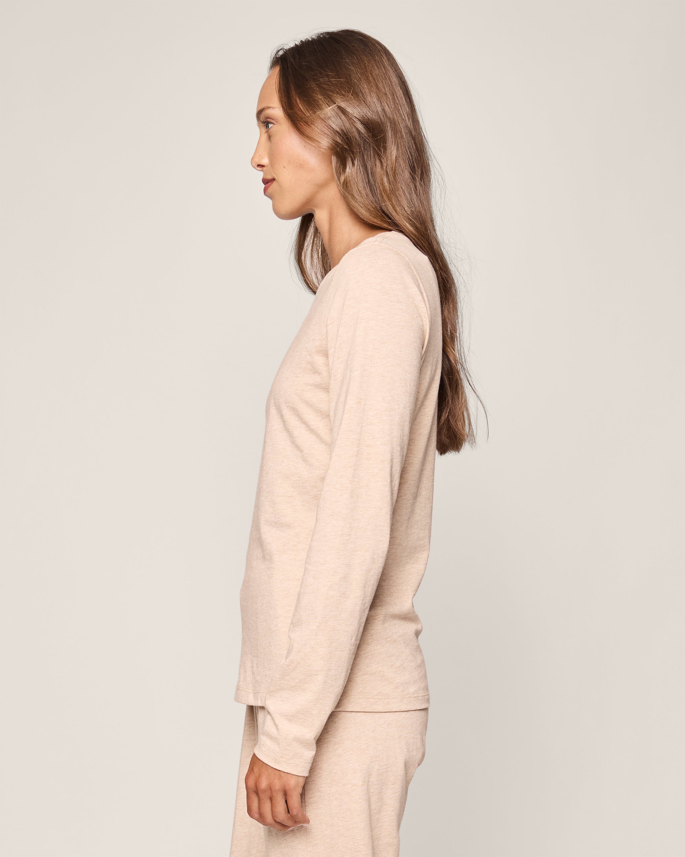 A person with long brown hair is standing in profile against a light gray background, wearing a Womens Pima Long Sleeve Top in Camel by Petite Plume, crafted from soft Peruvian Pima cotton, paired with matching pants.