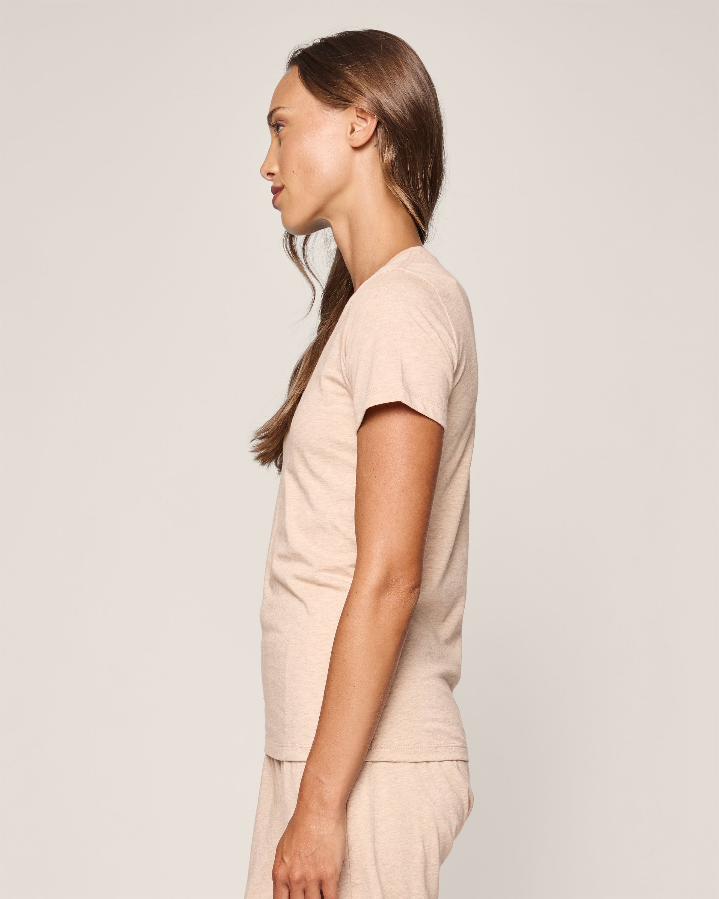 A person with long brown hair stands in profile against a plain background, wearing the luxurious Petite Plume Womens Pima Short Sleeve Top in Camel.