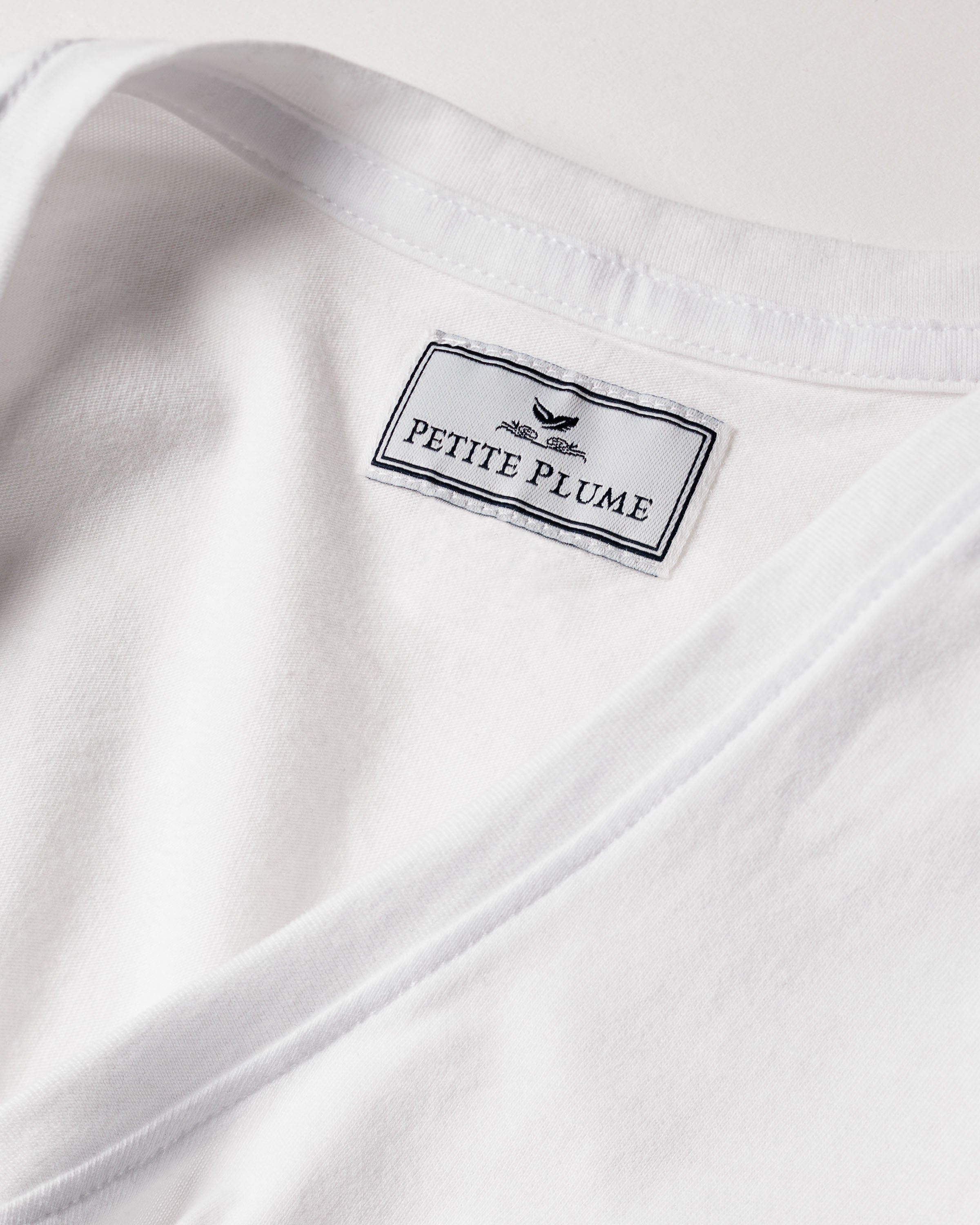 Close-up of a Womens Pima Short Sleeve Top in white by Petite Plume. Made from soft Peruvian Pima cotton, the label features a small bird illustration.