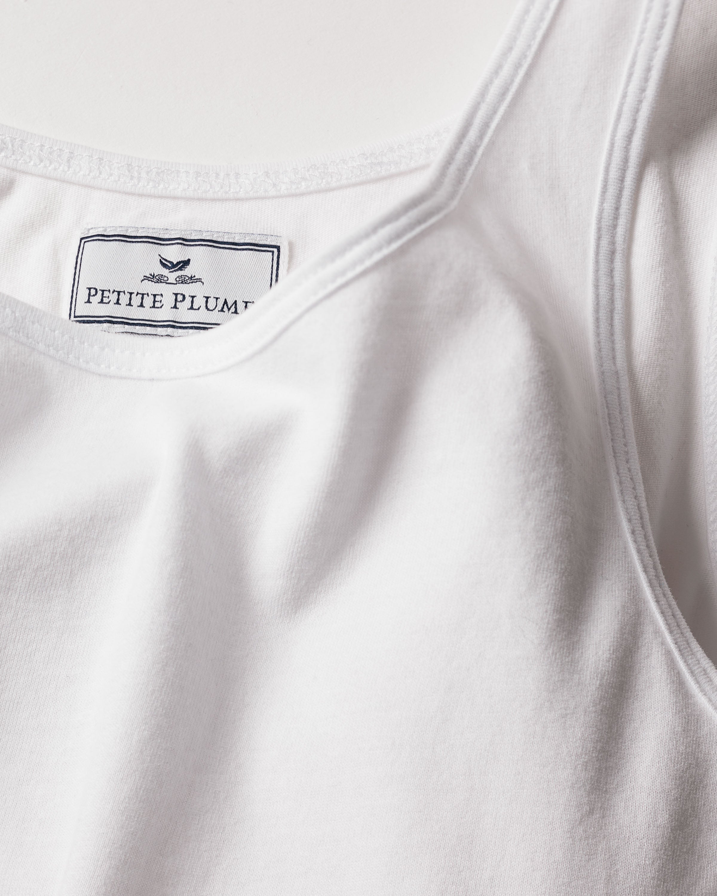 Close-up of the Womens Pima Tank Top in White, crafted from soft Peruvian Pima cotton. It features a Petite Plume label and simple bird logo inside the collar, highlighting its jersey knit texture and luxurious quality.