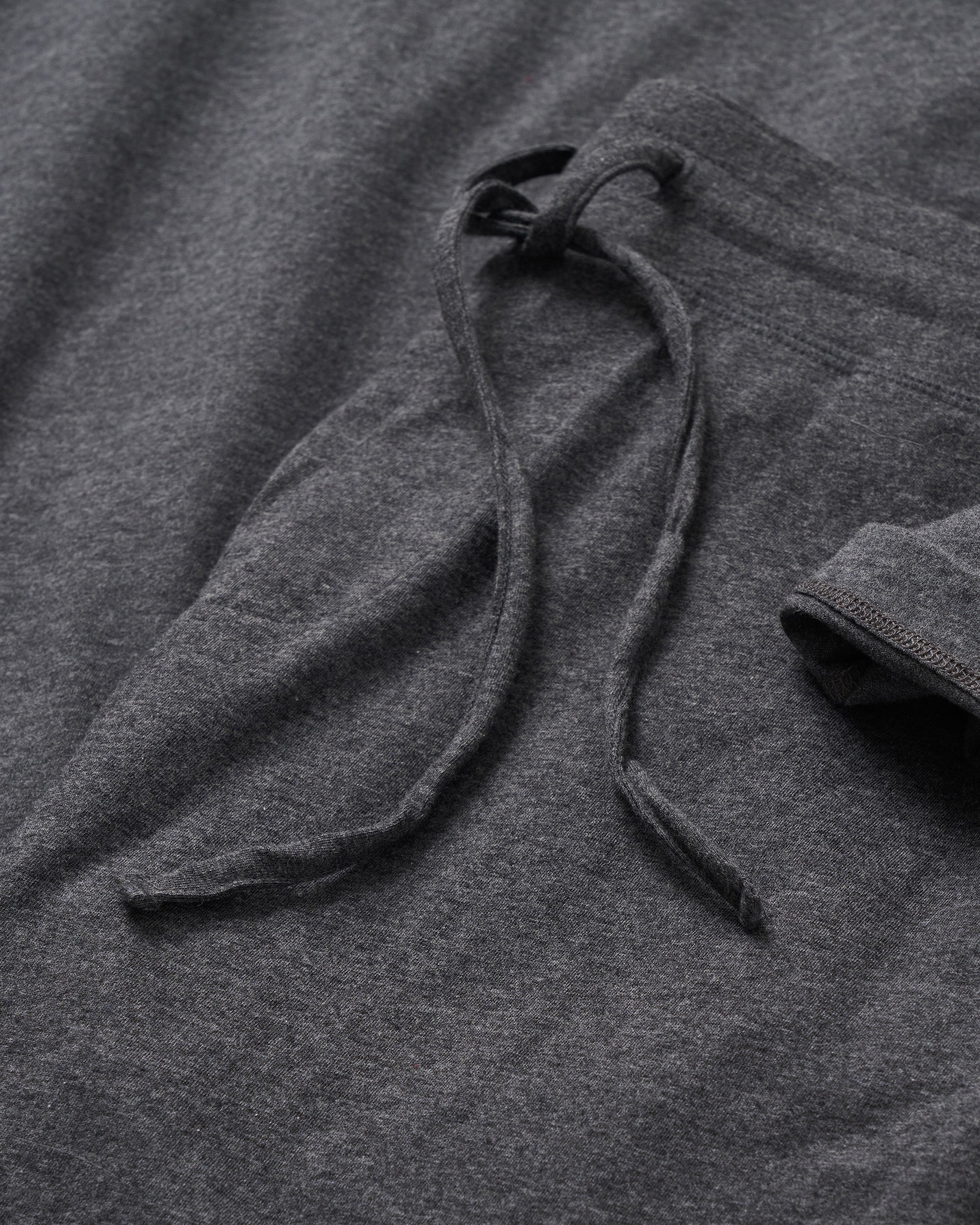 A close-up of Petite Plumes Mens Classic Pima Shorts in Dark Heather Grey shows their relaxed charm with a folded waistband and textured fabric, complemented by a casually draped yarn-dyed drawstring.