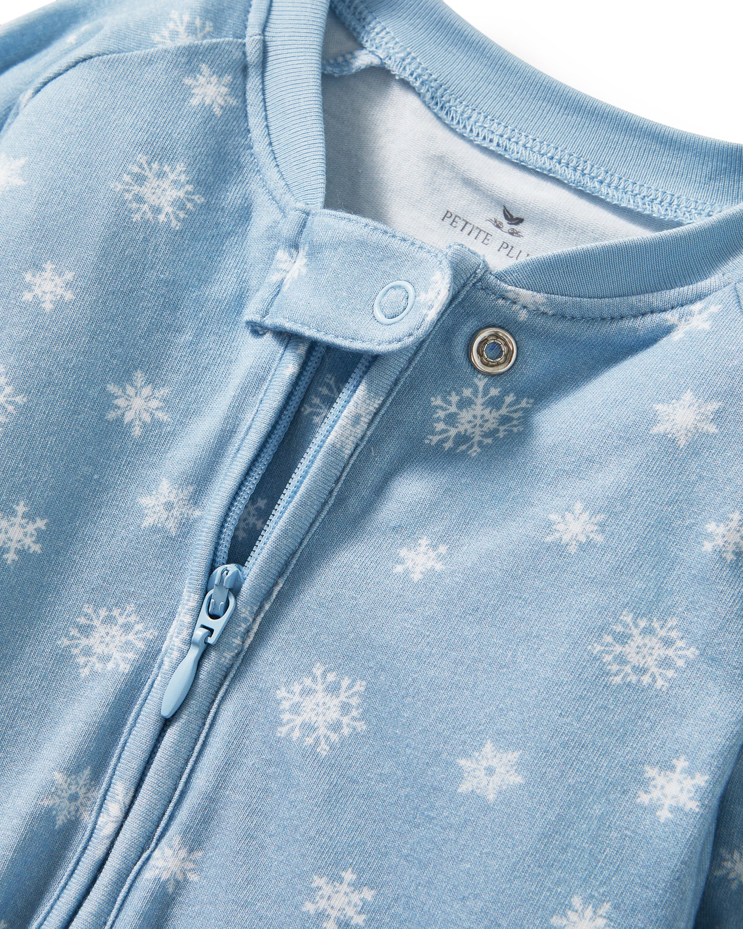 The Baby's Pima Peekaboo Romper in Periwinkle Wonderland features a light blue snowflake pattern, long sleeves with fold-over cuffs, and a diagonal zipper from neckline to left ankle; one sleeve and one leg are folded.
