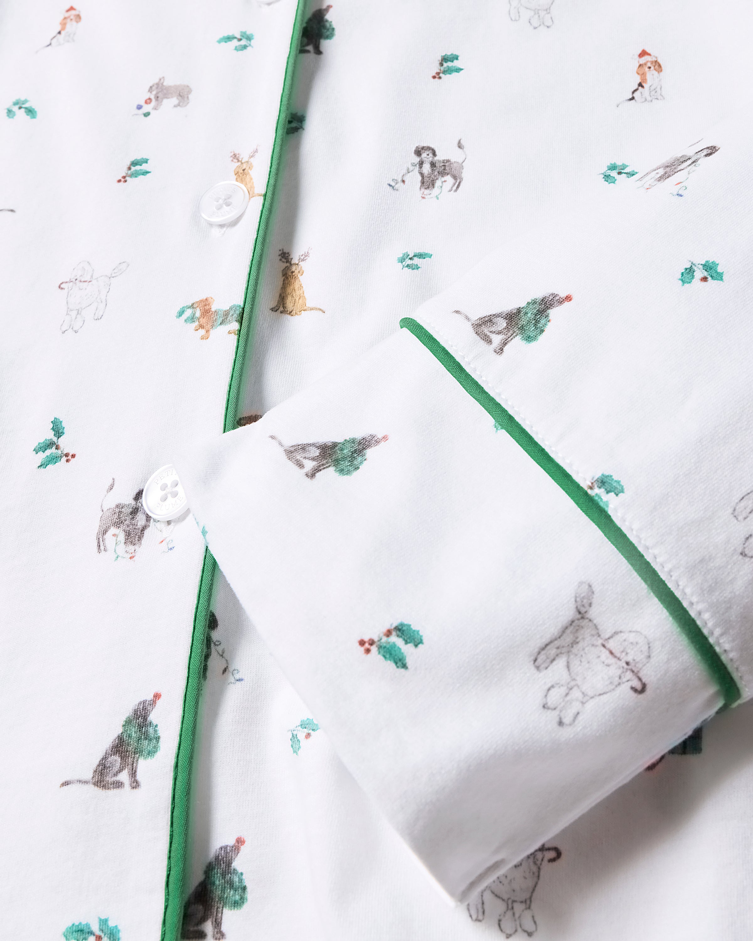 Close-up of Mens Pima Pajama Set in Jingle Paws by Petite Plume, showcasing a white pajama shirt with dog and tree illustrations. Made from luxurious Peruvian Pima cotton, it features green piping and white buttons for comfort and style, perfect holiday sleepwear.