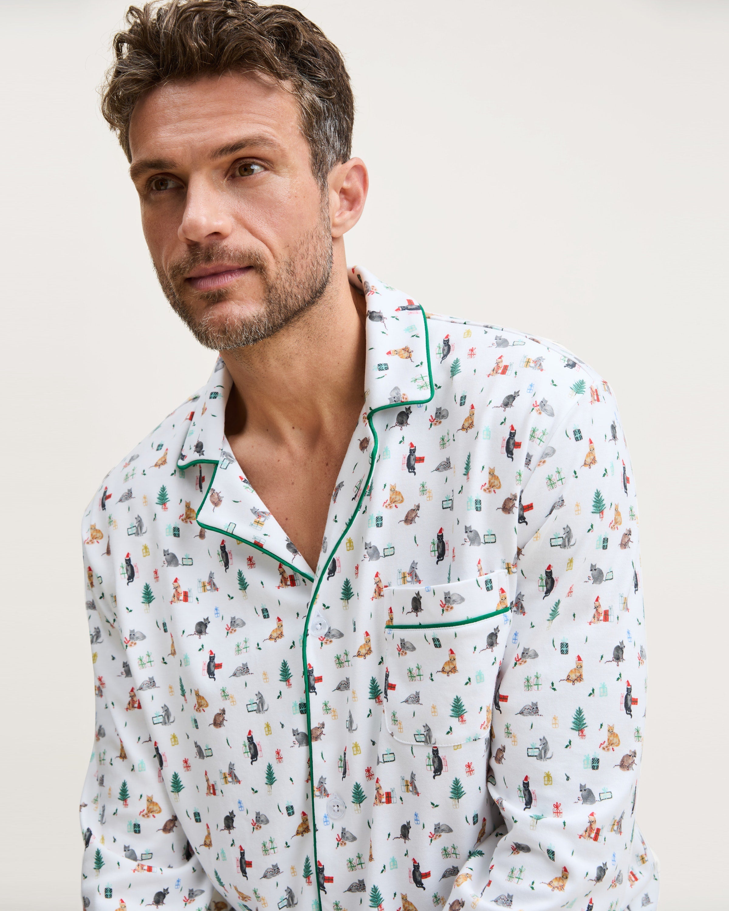 Men's Pima Pajama Set in Merry Meow: white set with green piping, featuring an all-over print of playful colorful cats. Includes a long-sleeve button-up shirt with chest pocket and matching pants.