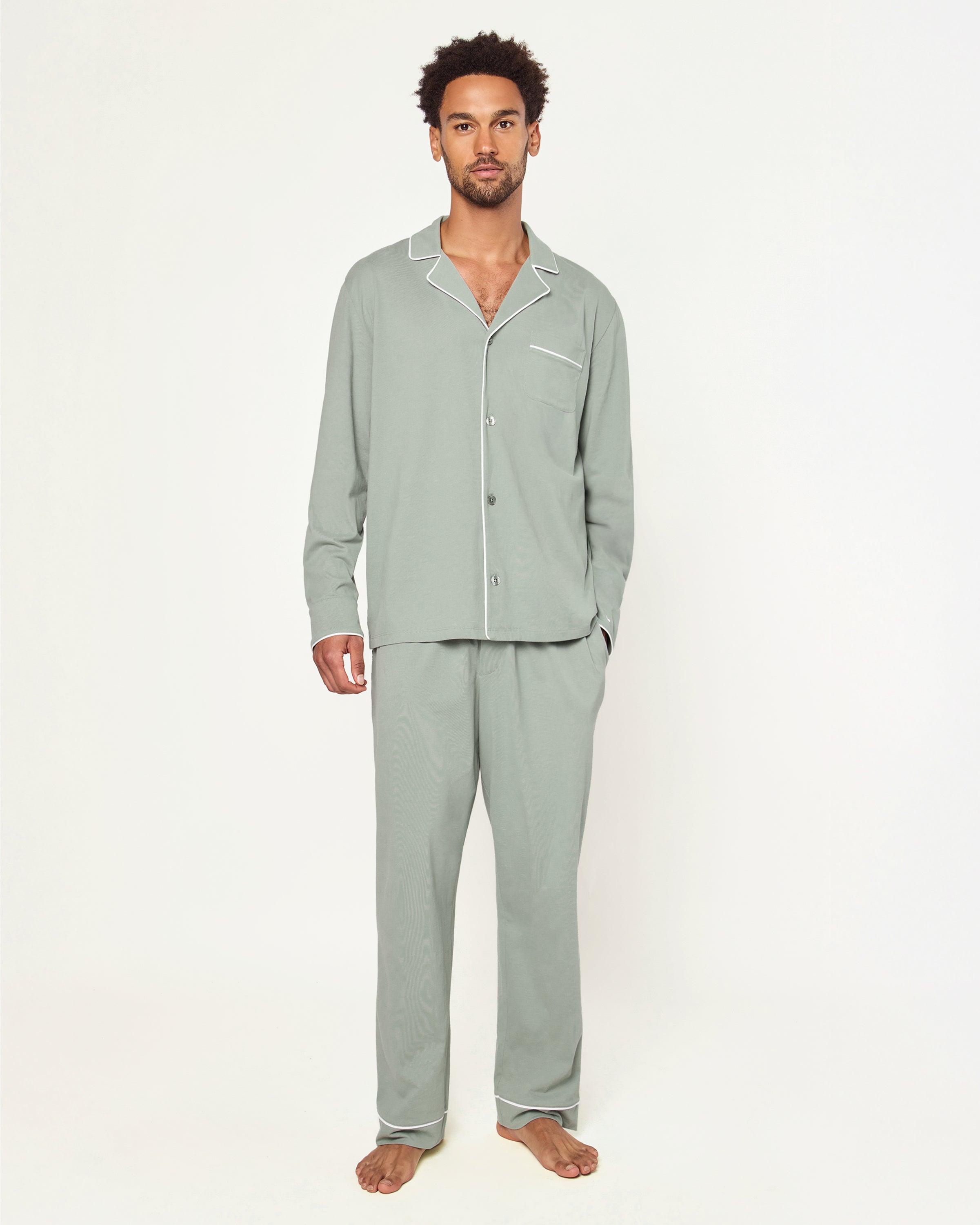 Men’s Pima Pajama Set in Sage: long-sleeve button-up top with white piping and chest pocket, plus matching drawstring pants, both laid flat on a white background.