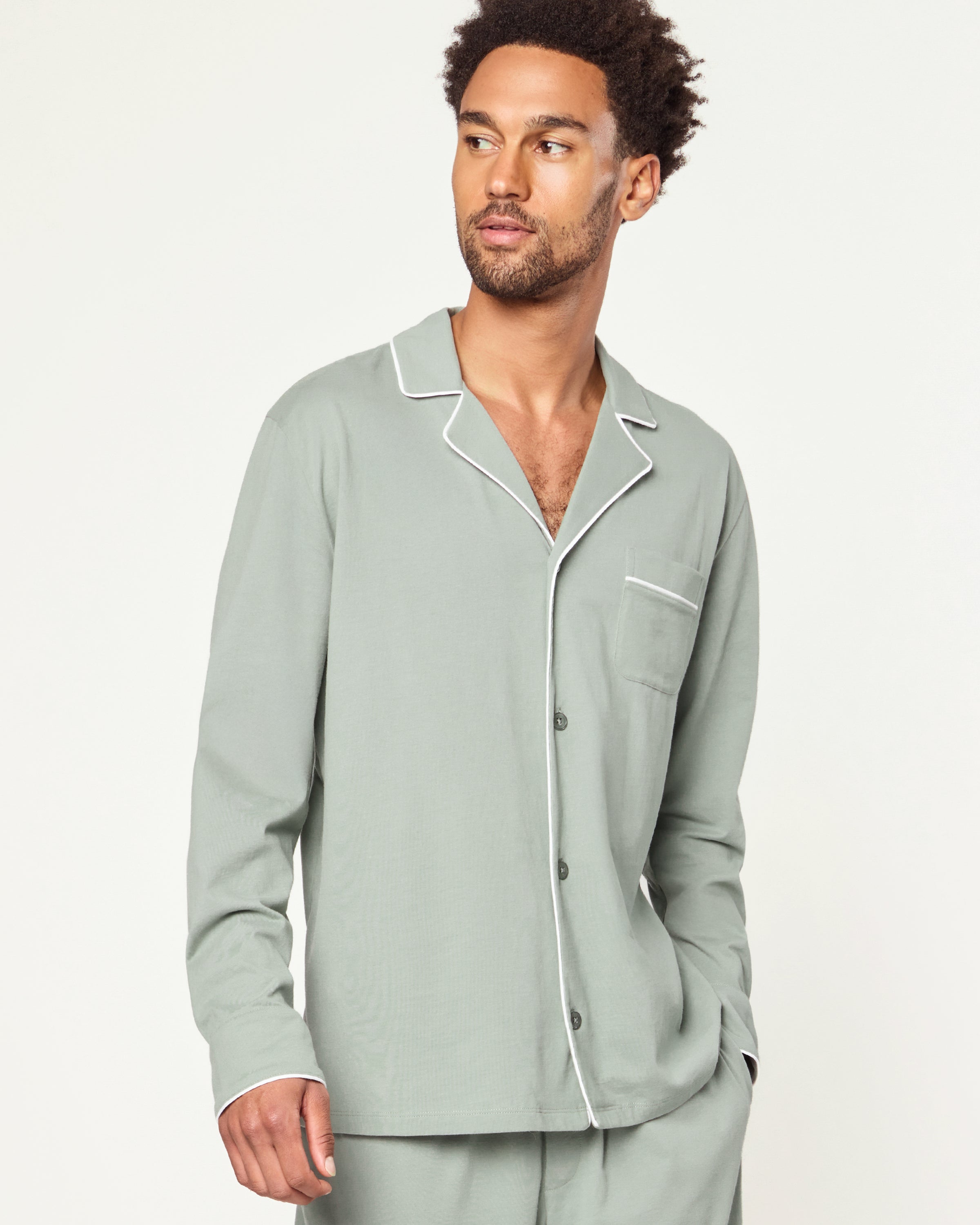 Men’s Pima Pajama Set in Sage: long-sleeve button-up top with white piping and chest pocket, plus matching drawstring pants, both laid flat on a white background.