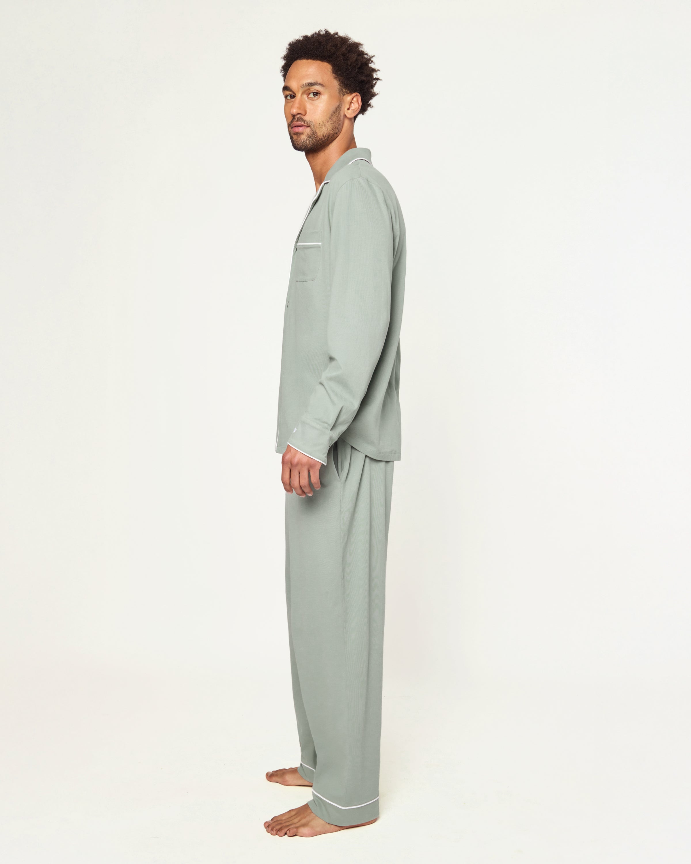 Men’s Pima Pajama Set in Sage: long-sleeve button-up top with white piping and chest pocket, plus matching drawstring pants, both laid flat on a white background.
