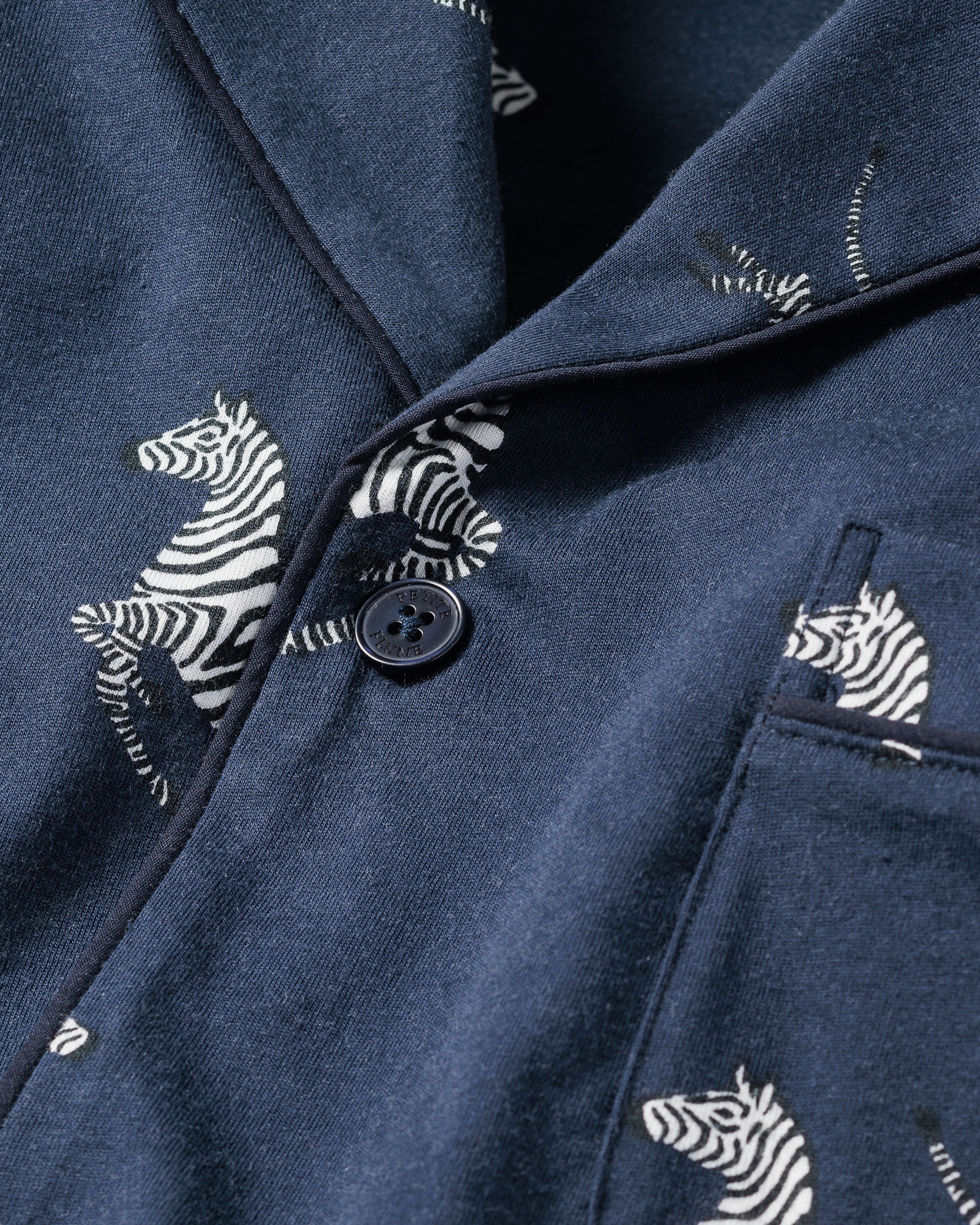 Close-up of the Mens Pima Pajama Set in Zèbre de Nuit by Petite Plume shows premium navy Pima cotton with a button, featuring a charming zebra print pattern and a small pocket on the right.