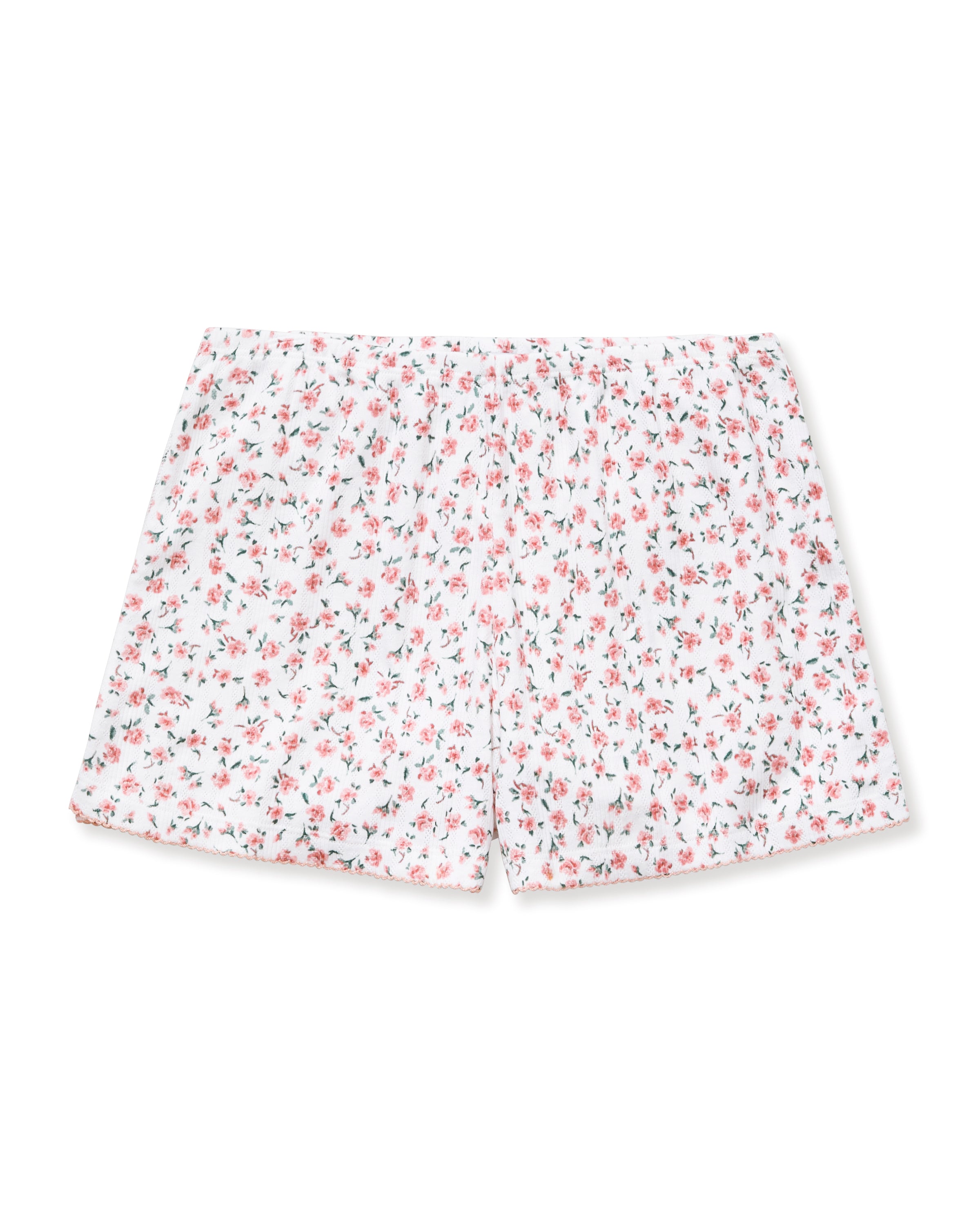 A woman with long curly hair and a relaxed expression stands barefoot against a neutral background, wearing Women's Pointelle Shorts in Pink Floral as part of a matching short-sleeved pajama set.