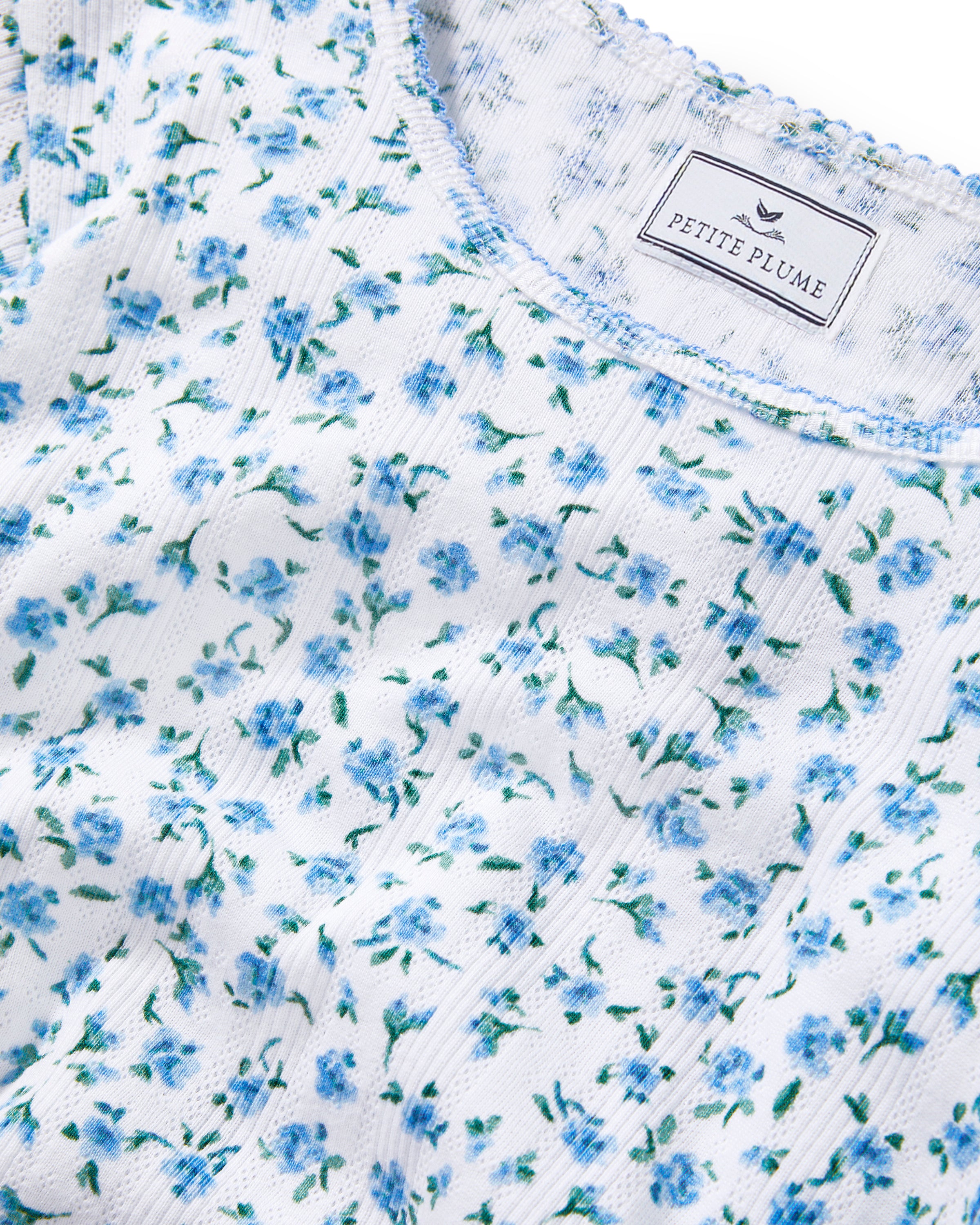 A young woman with long curly brown hair wears the Women's Pointelle T-Shirt in Blue Floral, paired with a matching skirt, against a plain light background.