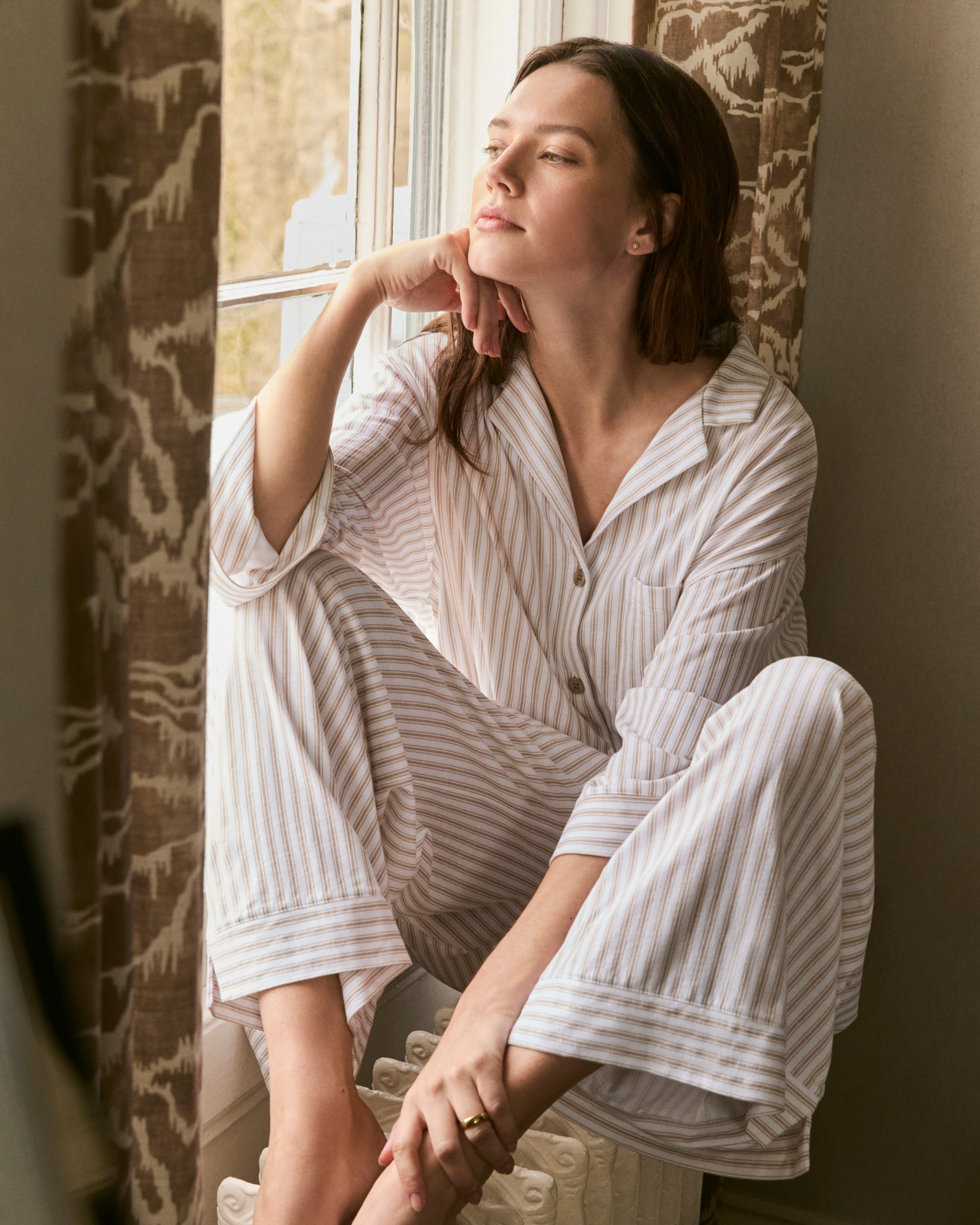 The Olivia Wide Leg Pima Pajama Set in Camel Ticking features light-colored, long-sleeve striped pajamas with brown buttons and matching drawstring pants, displayed flat on a white background.