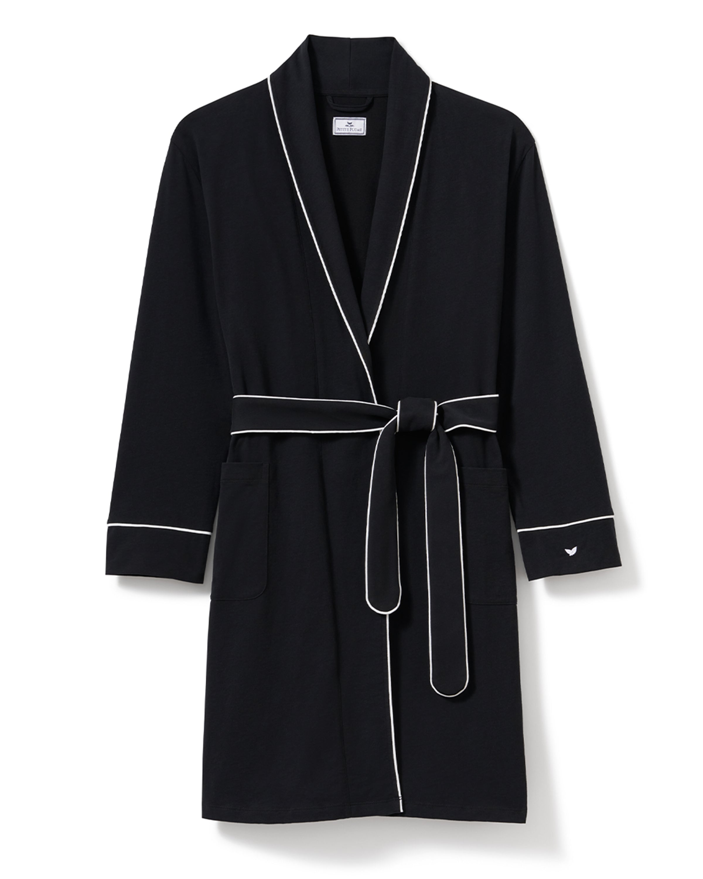 A woman wears a Petite Plume Womens Pima Robe in Black, characterized by white piping, long sleeves, and a waist tie. Made from soft Peruvian Pima cotton, she rests her hands in the front pockets while standing against a plain light gray background.