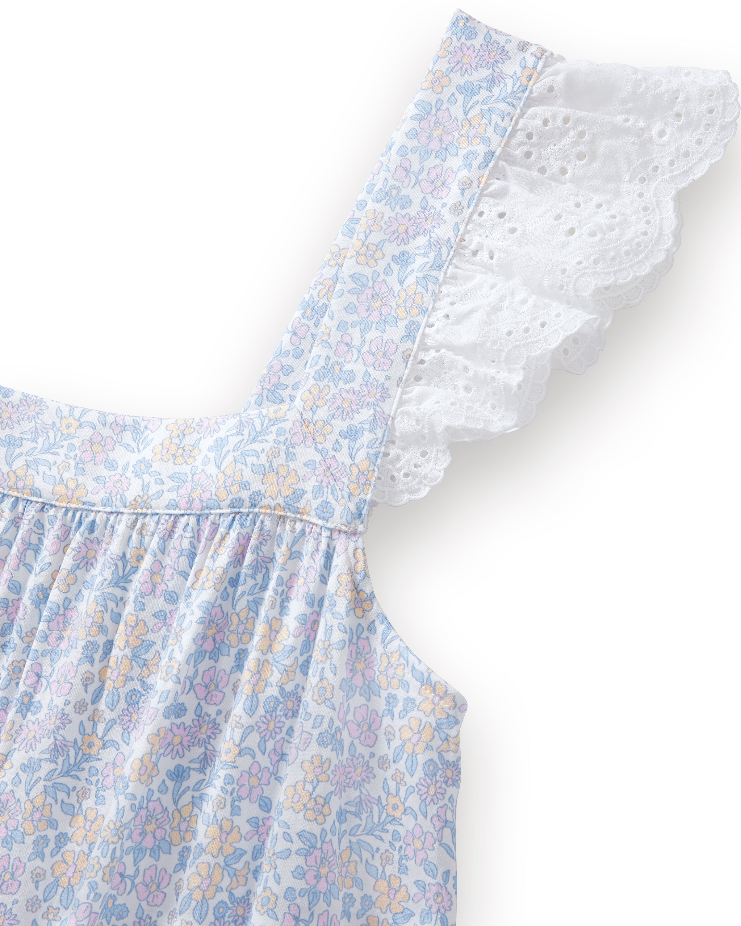 A woman with long curly hair stands barefoot on a plain light background, wearing the Women's Lightweight Pima Clara Nightgown in Fleur Blanche—an ankle-length, sleeveless gown with dainty floral print and lace-trimmed straps.