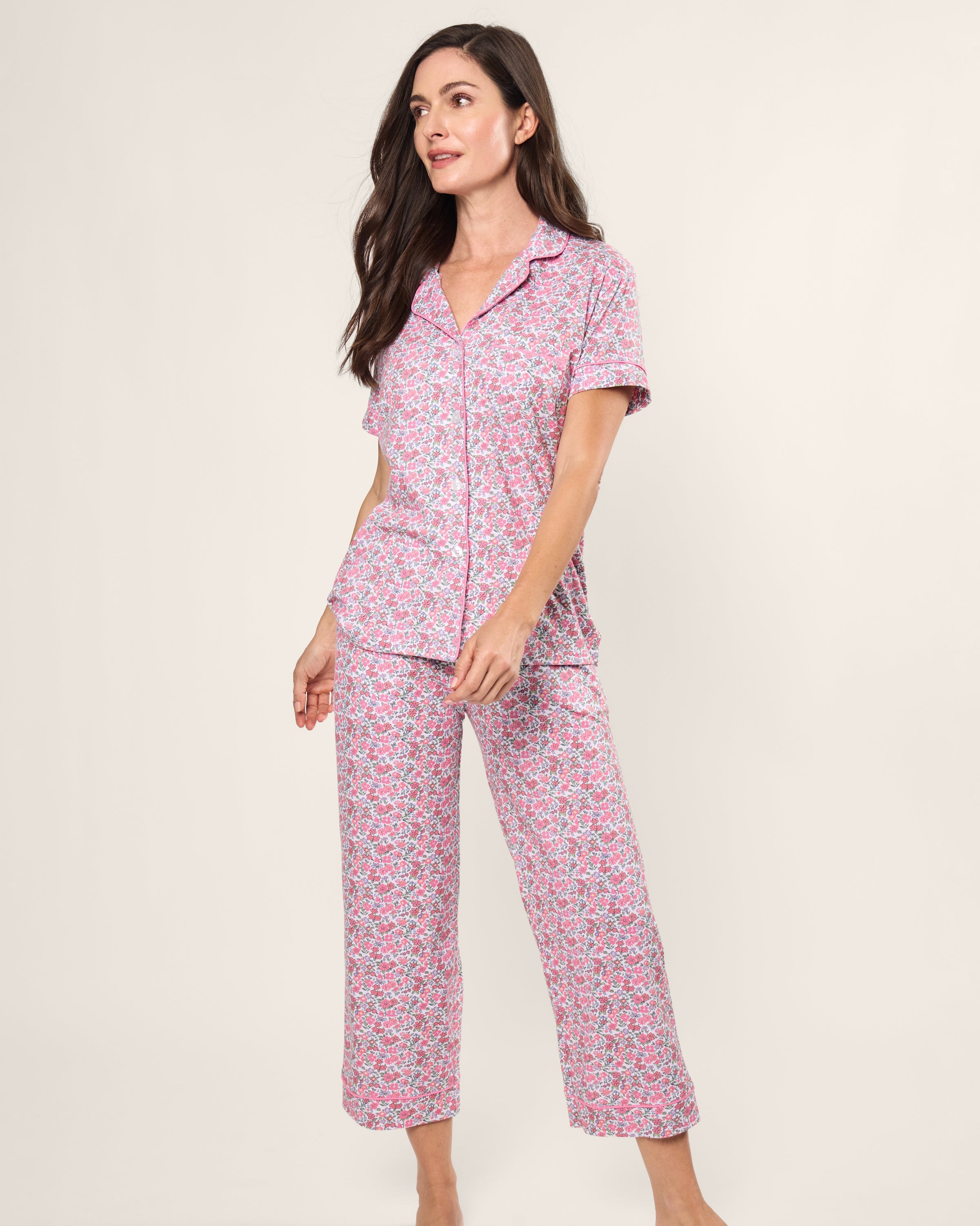 A person with long, dark hair poses against a plain background in Petite Plumes Womens Pima Crop Set in Fleurs de Rose, featuring a vintage pink and white floral pattern with short sleeves and cropped pants. The individual looks slightly to the side.