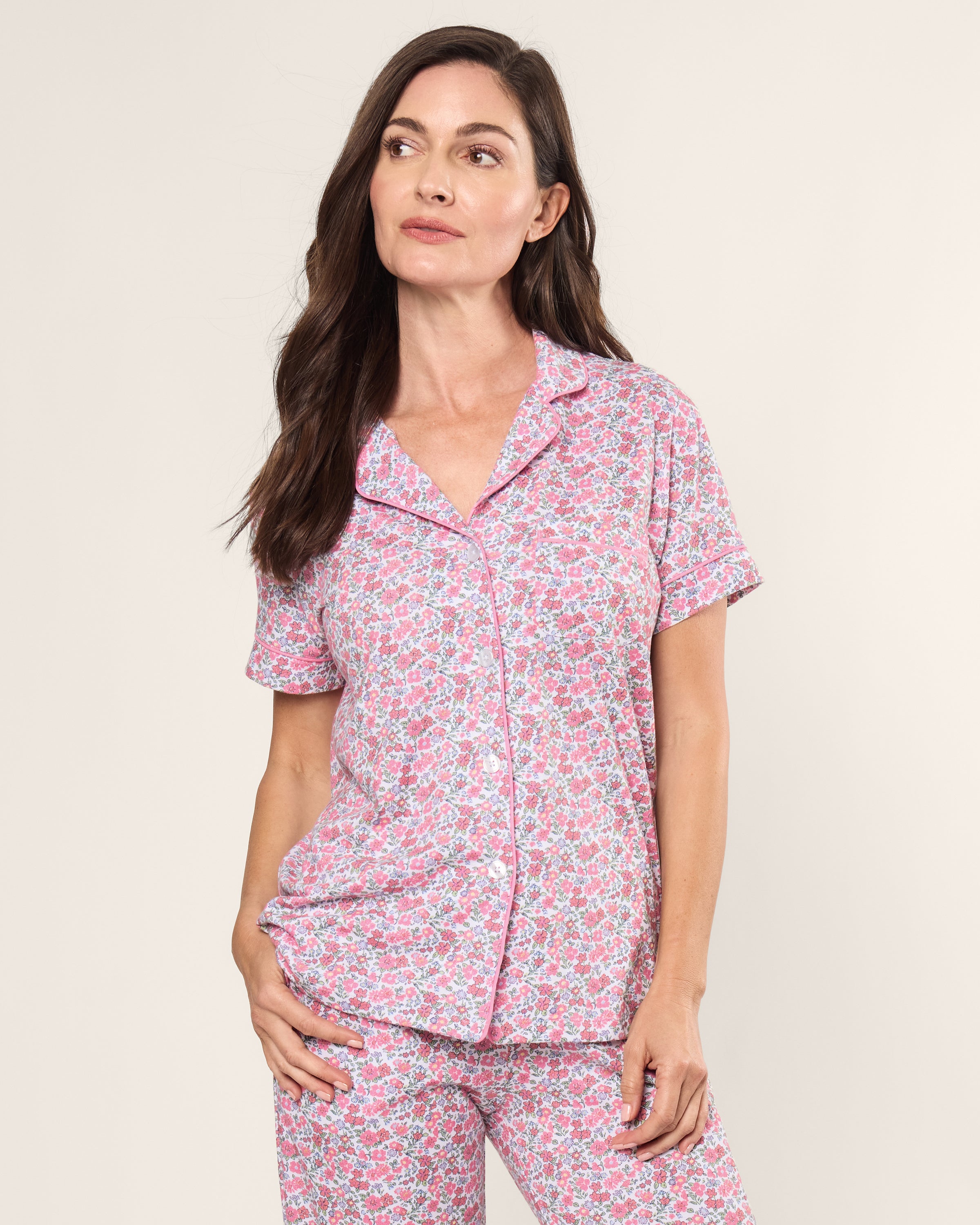 A person wearing Petite Plumes Womens Pima Crop Set in Fleurs de Rose, featuring breathable Pima cotton with short sleeves and a collar. They have long dark hair, standing against a light background with a relaxed expression.