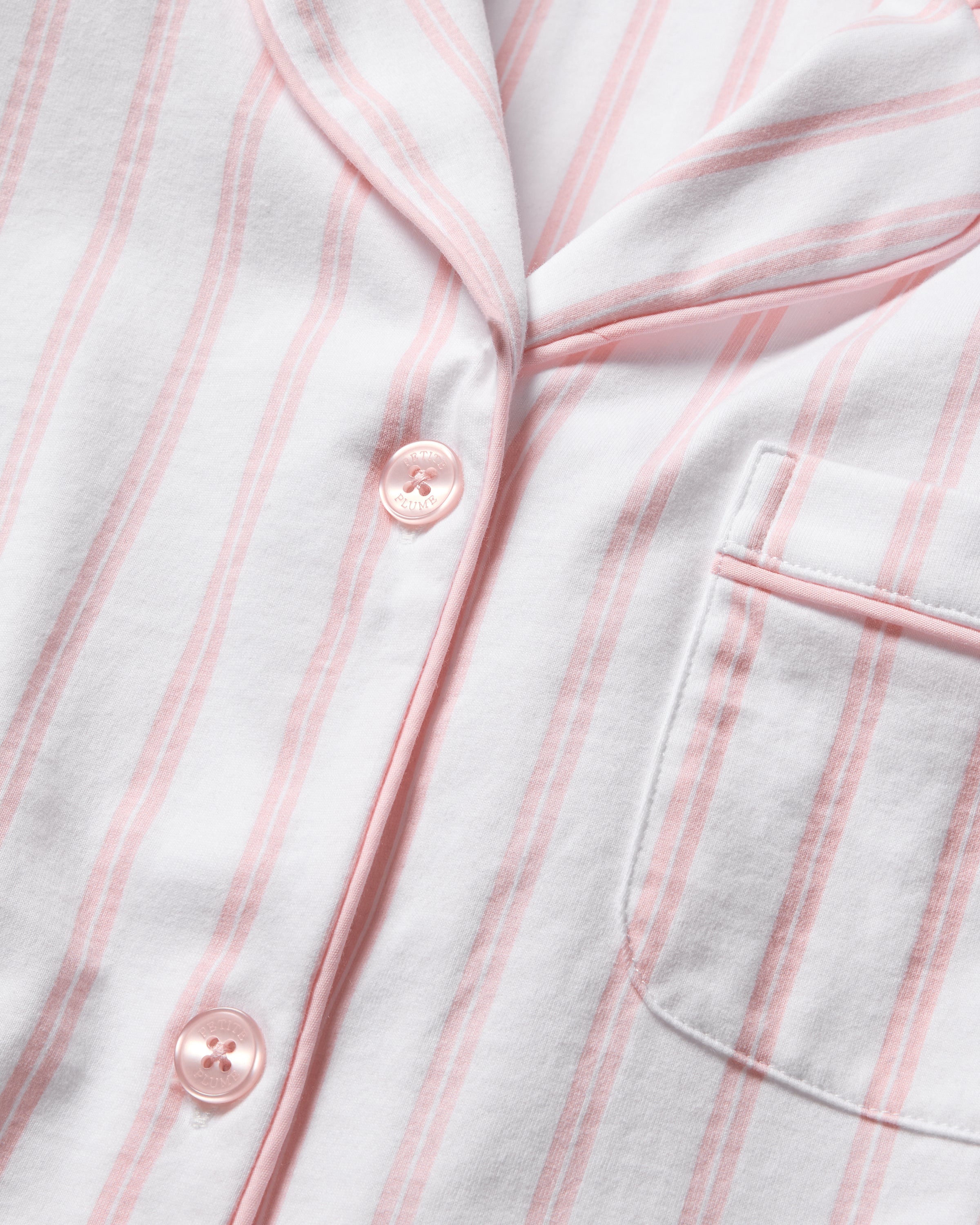 A close-up of Petite Plumes Womens Pima Pajama Short Set in Pink Stripe shows a white pajama shirt with pink stripes, crafted from soft Peruvian Pima cotton. It features pink buttons and a right chest pocket, embodying luxury pajamas.